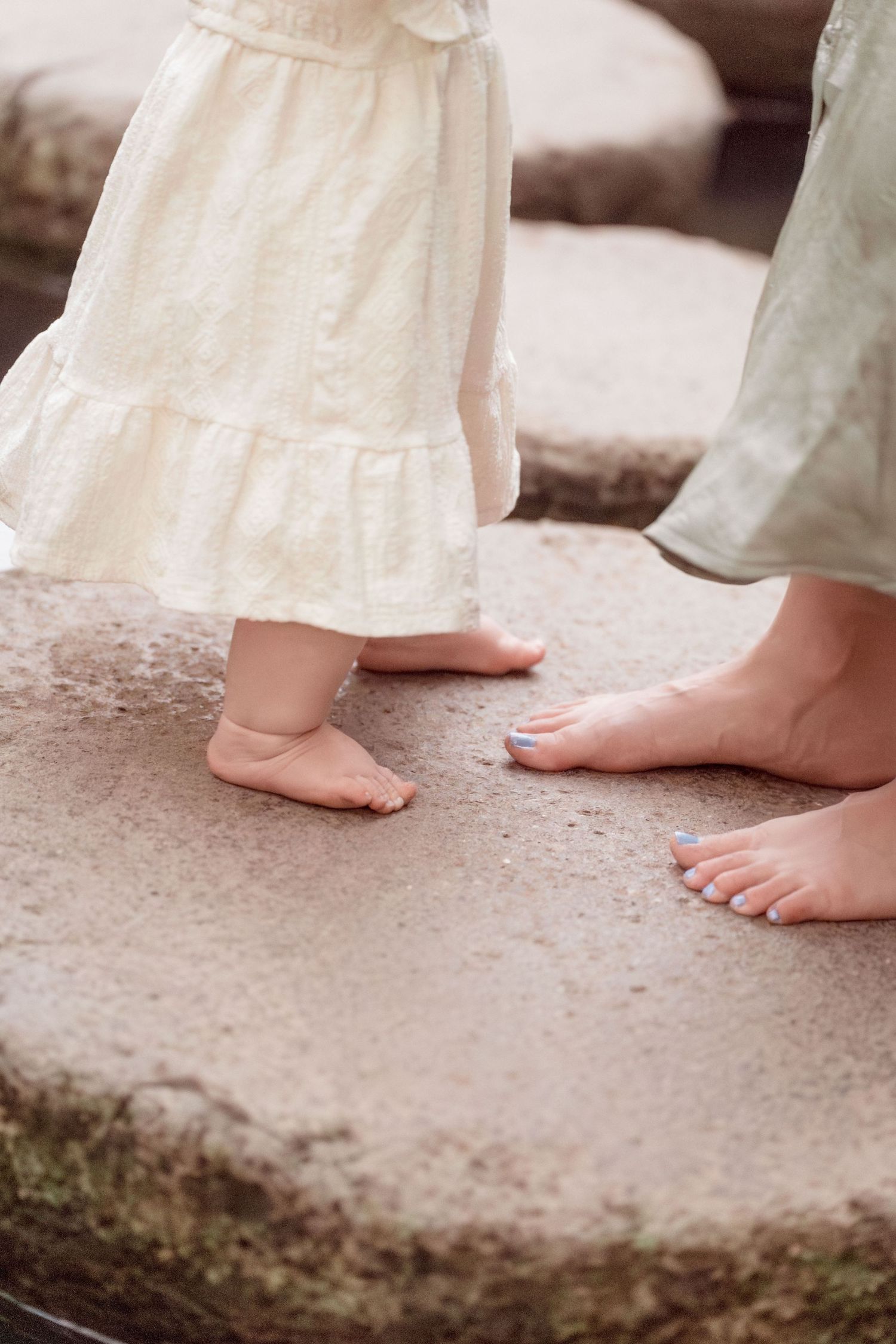 Close-up of barefoot baby and mother standing together on a stone surface outdoors.