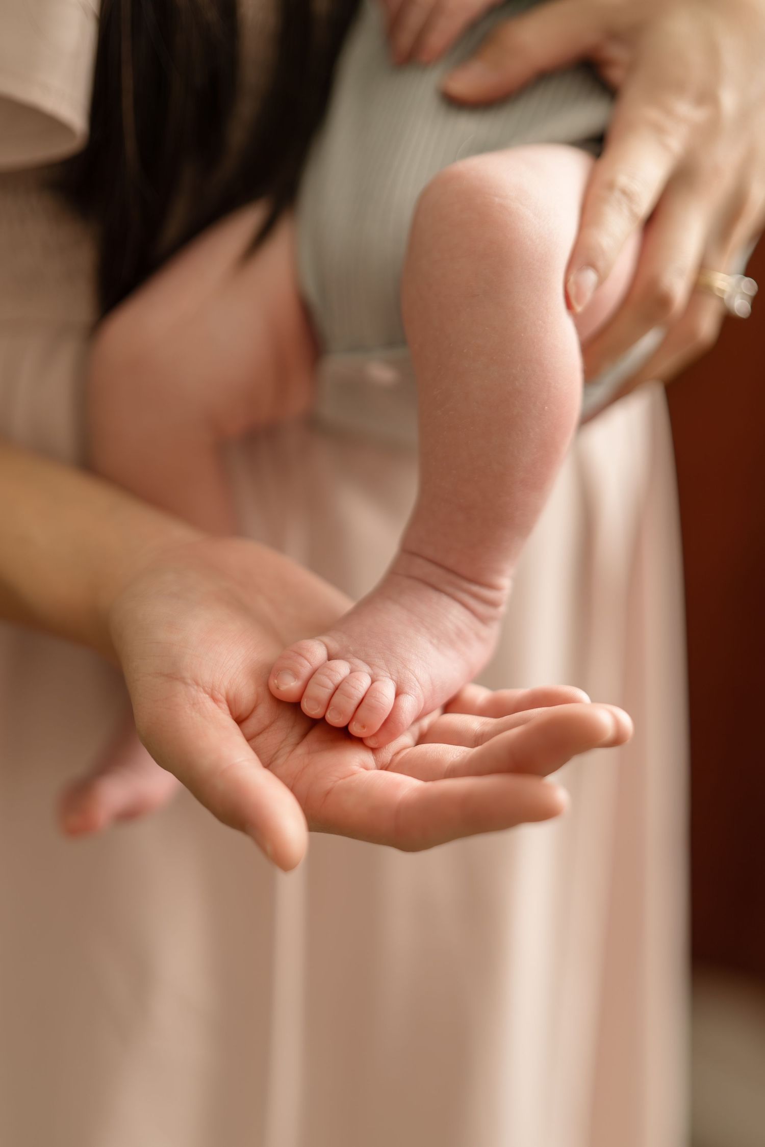 Close-up of newborn baby tiny feet resting in mothers open palm, baby wearing sage green onesie.