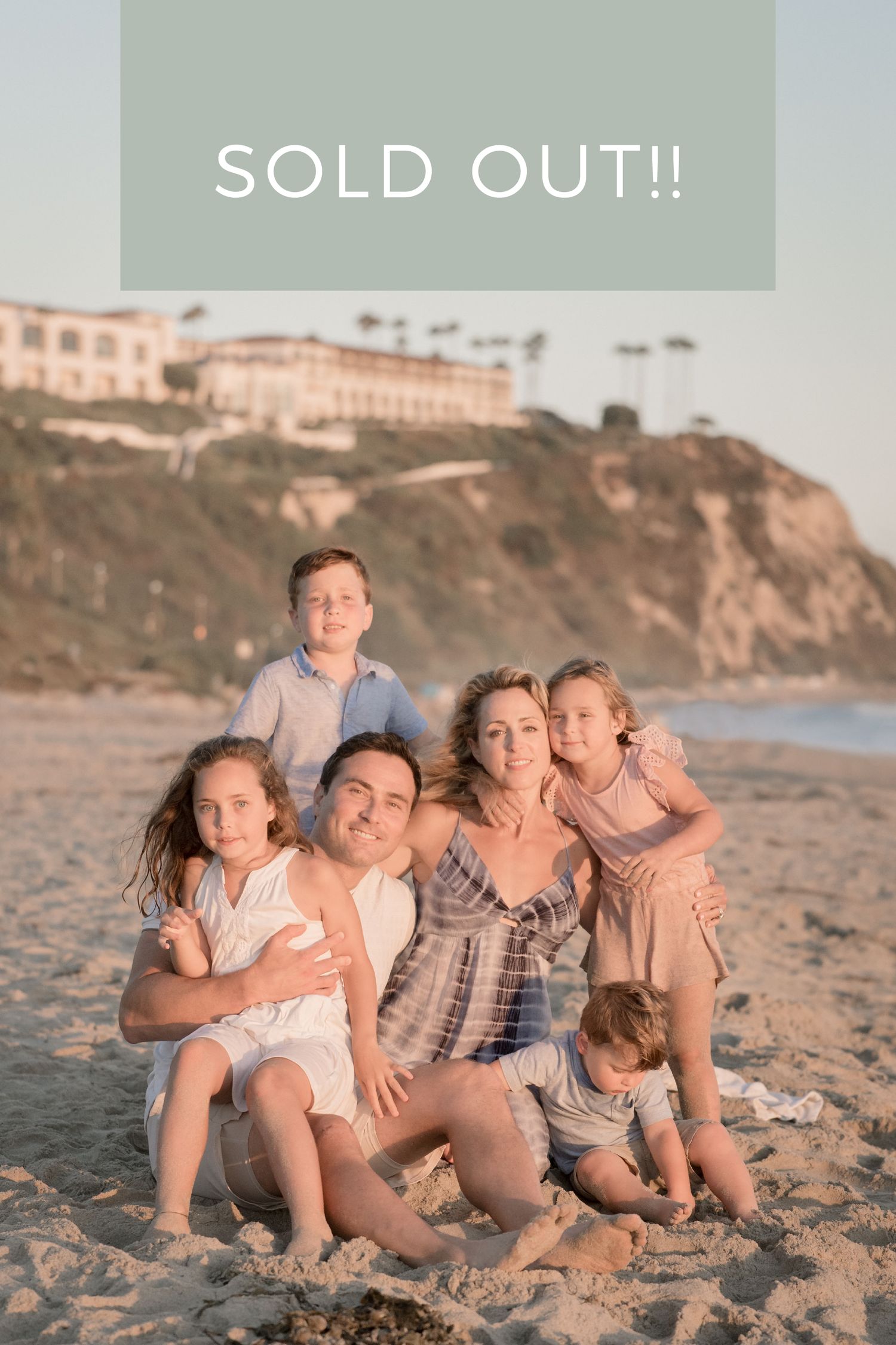 Family of six posing together on sandy beach at sunset with coastal cliffs behind them.