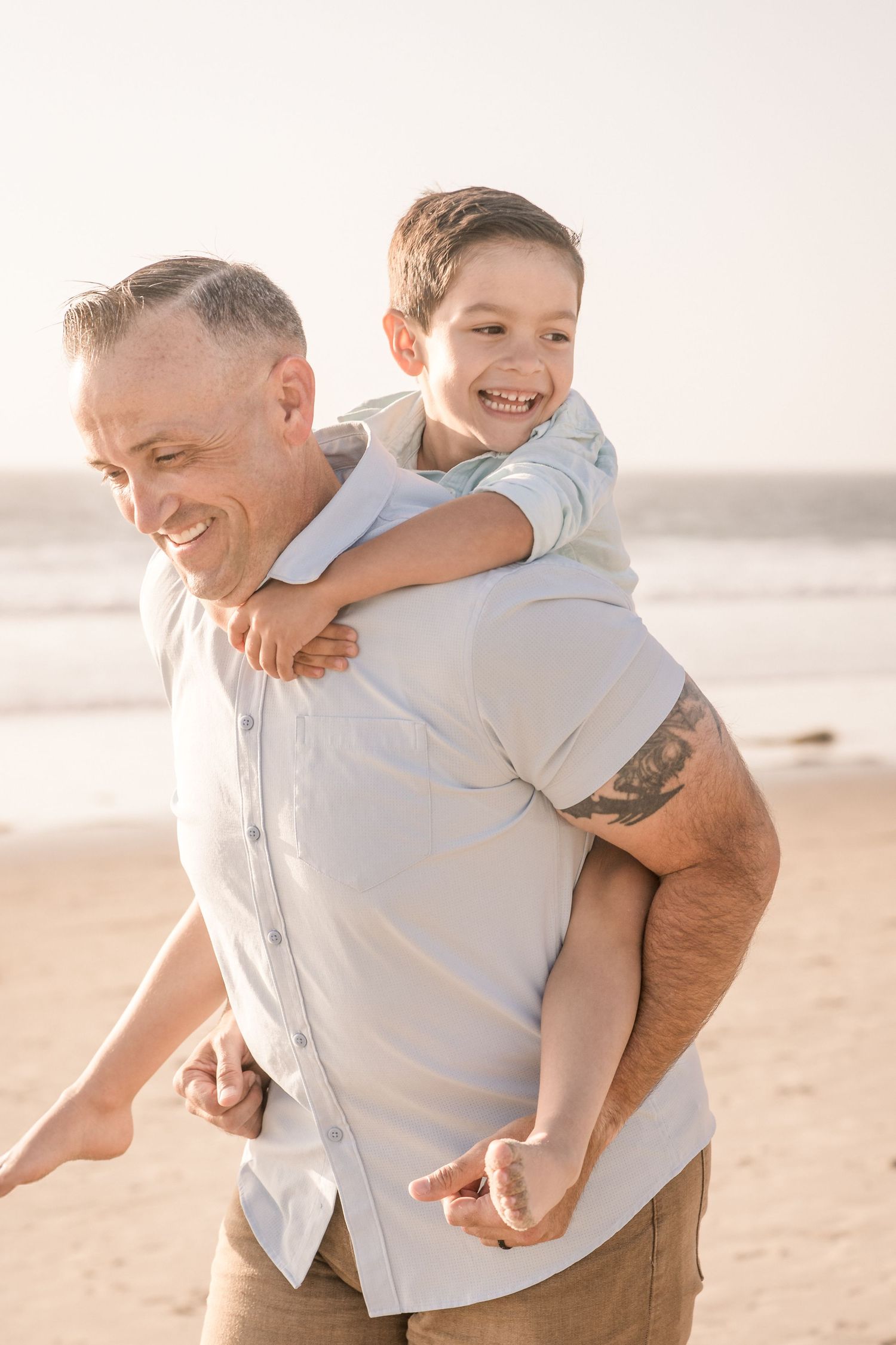 Smiling father giving his laughing young son a piggyback ride on a sunny beach.