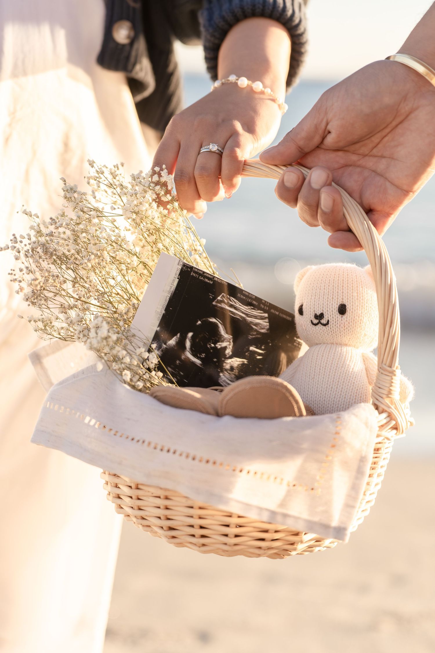 Couple holding wicker basket with ultrasound photo, stuffed bear, and dried flowers for pregnancy announcement.