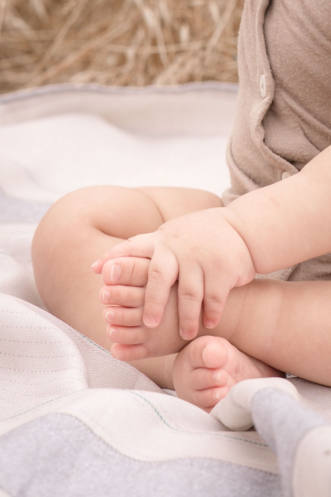 Close-up of a baby's tiny feet and hands resting on a soft white blanket outdoors.
