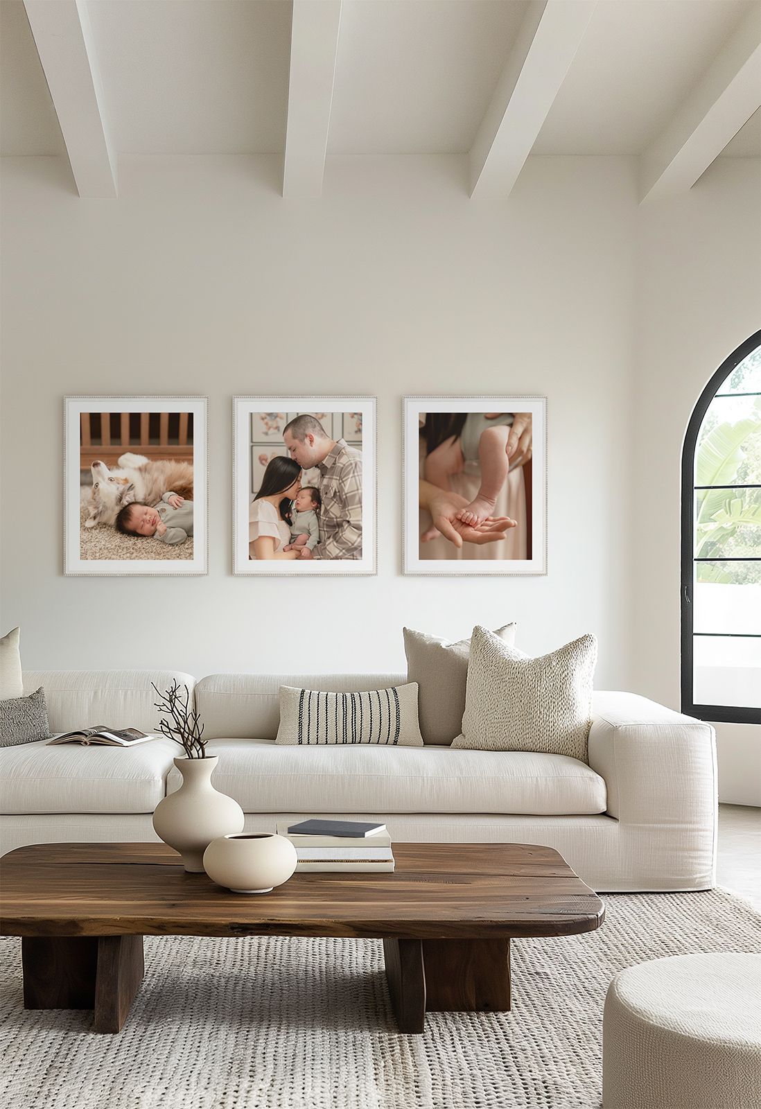 Modern minimalist living room with white sofa, wood coffee table, and three framed family photos on a white wall.