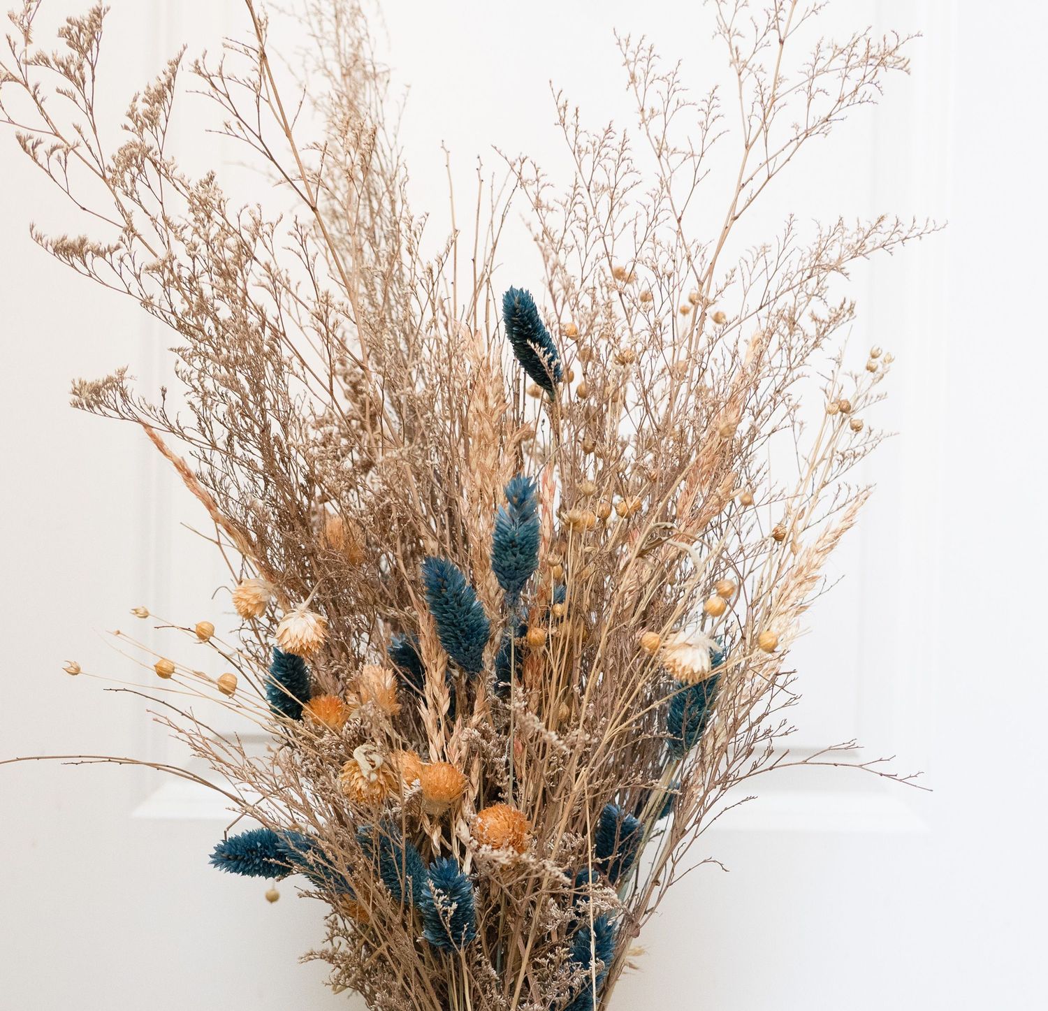 Bohemian dried flower arrangement featuring teal bunny tails, golden grasses, and orange blooms.