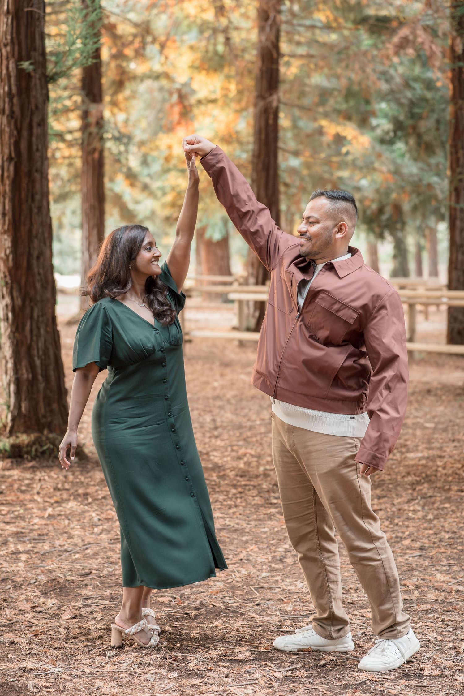 A couple dances joyfully together in a redwood forest, the man raising the womans hand gracefully.