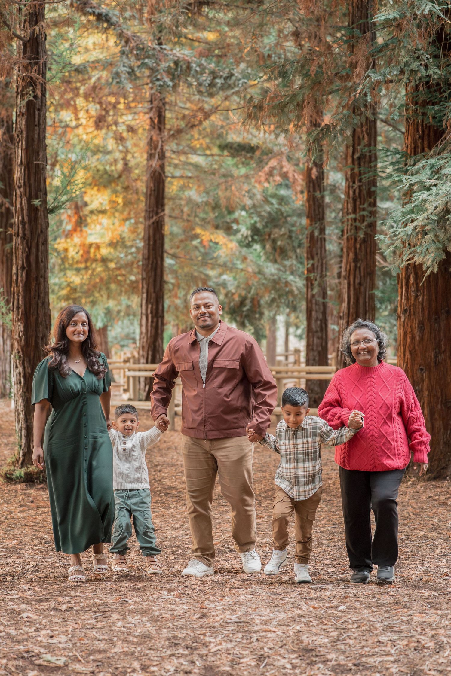 A multigenerational family of five walks hand-in-hand through a redwood forest in autumn.