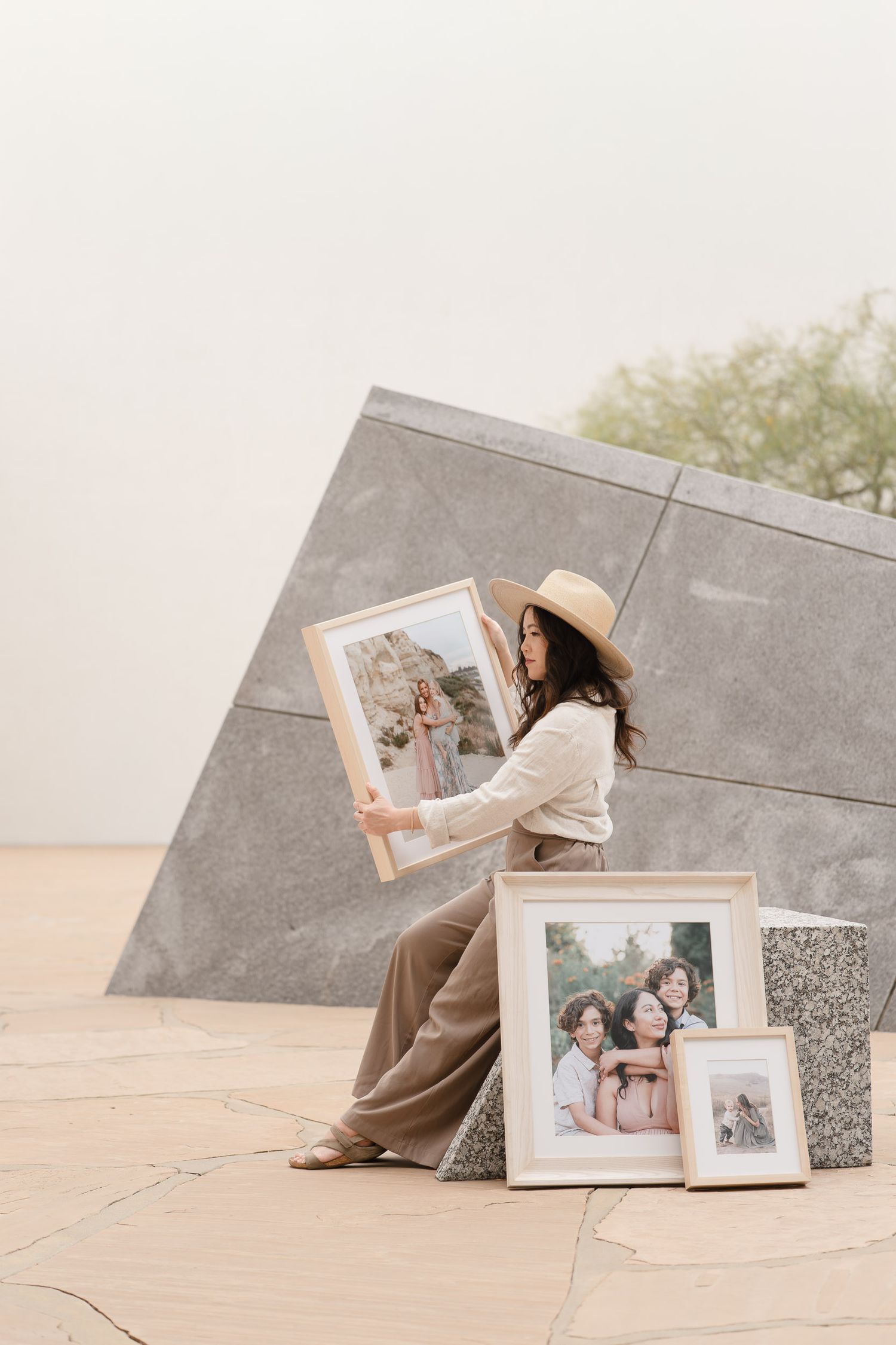 Woman in a straw hat holding a framed photo outdoors, with more framed portraits displayed nearby.