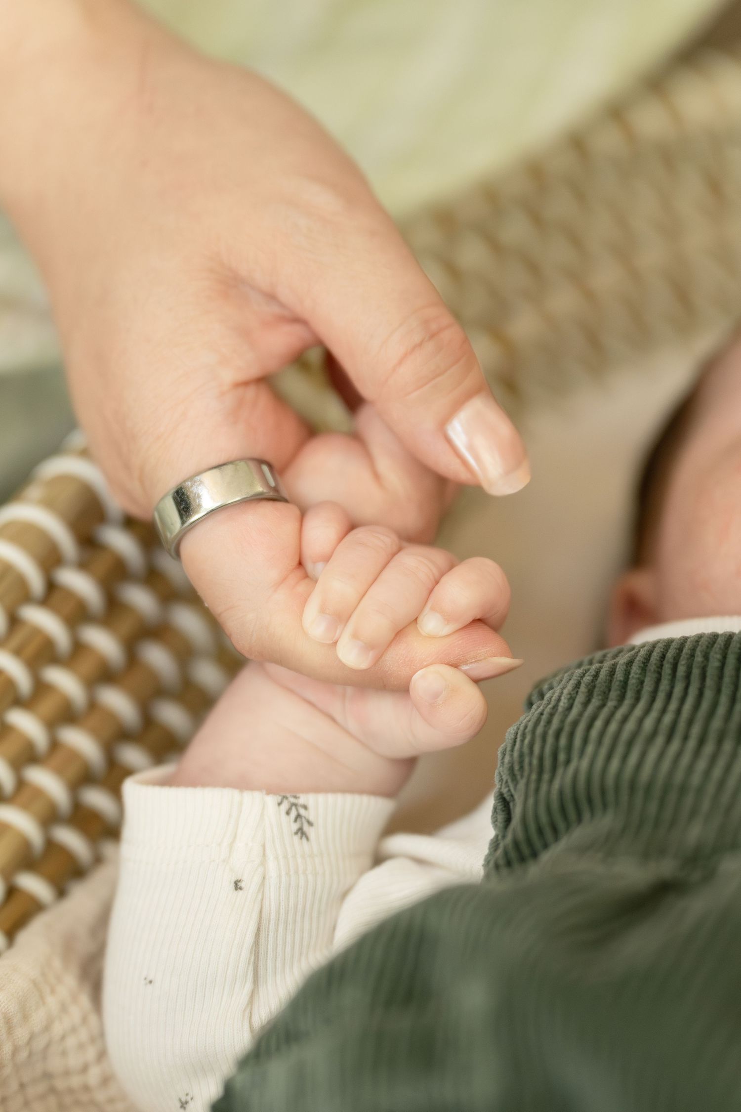 Close-up of newborn baby grasping mothers finger, mother wearing silver ring, baby in green corduroy outfit.