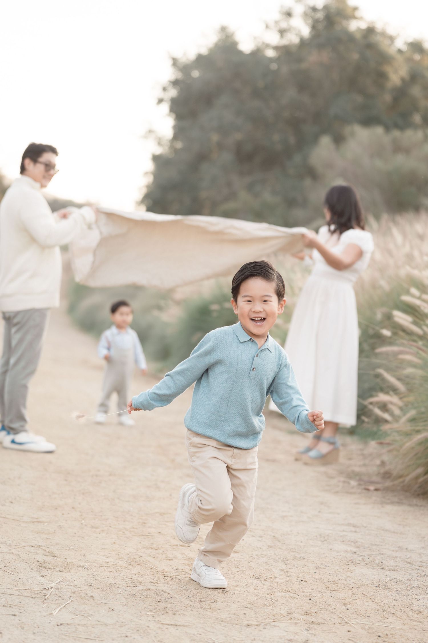 A joyful young boy runs toward the camera while his family holds a blanket in a scenic outdoor setting.