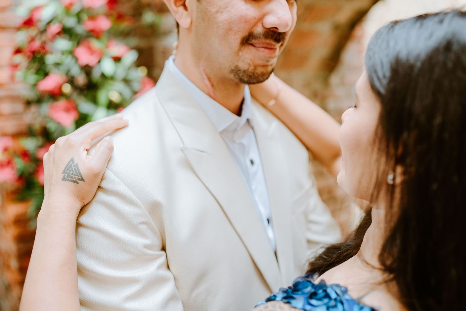 A couple shares a tender moment, the groom in a white suit smiling as his partner places her hand on his shoulder.