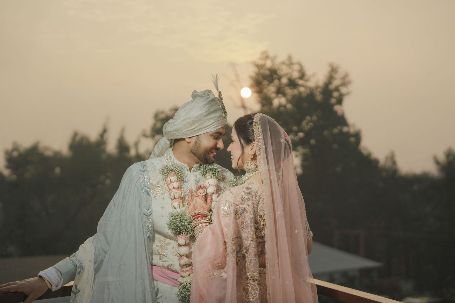 A couple in pastel outfits embraces in a romantic outdoor setting during golden hour.
