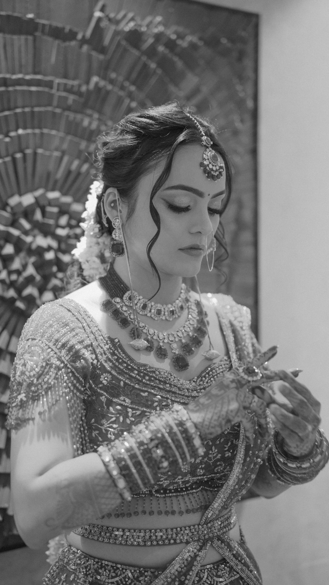 Black and white photo of a bride in traditional Indian bridal lehenga with jewelry and floral hair accessories.