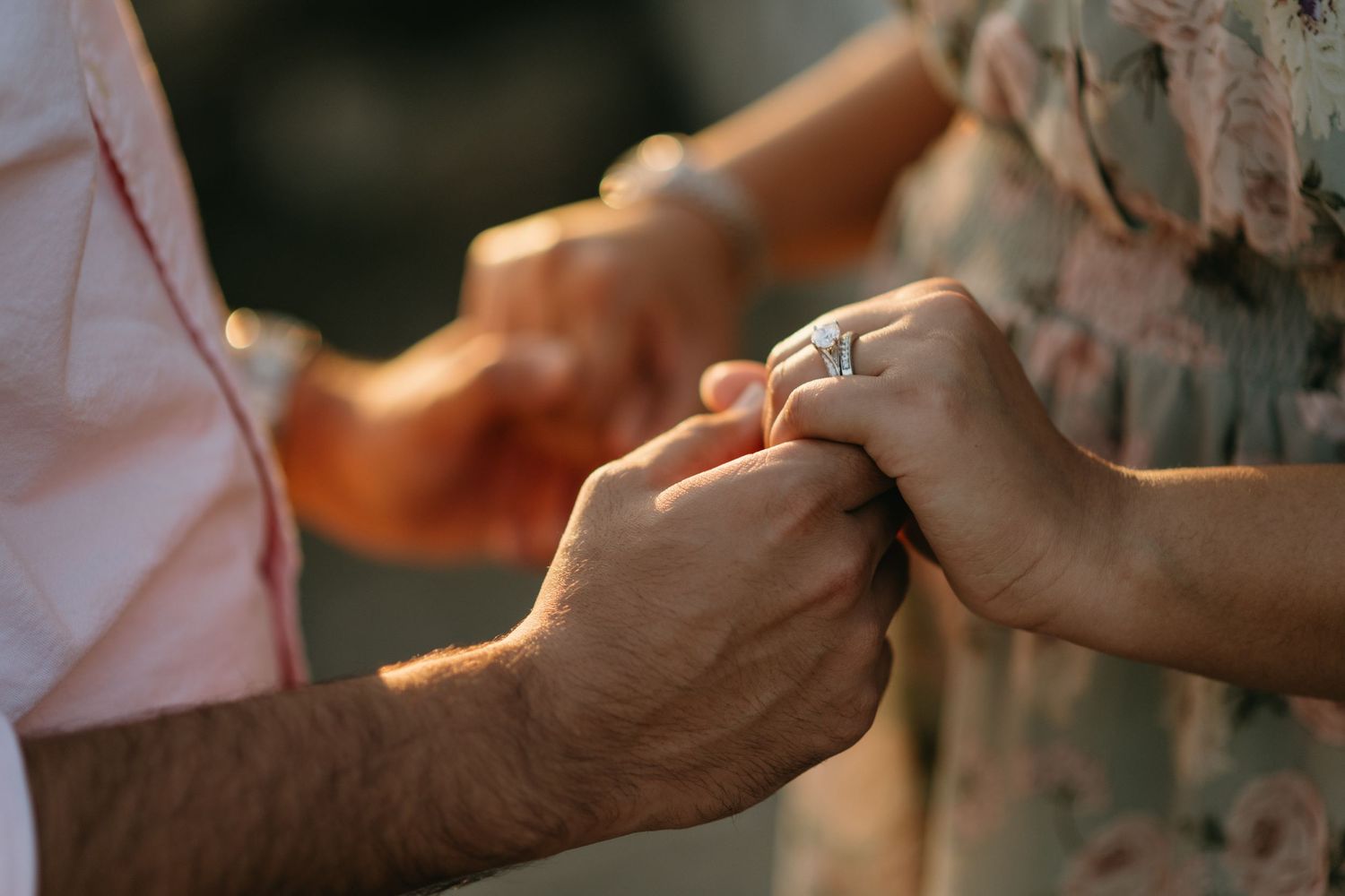 Close-up of a couple holding hands during a marriage proposal, with a sparkling diamond engagement ring on the womans finger.