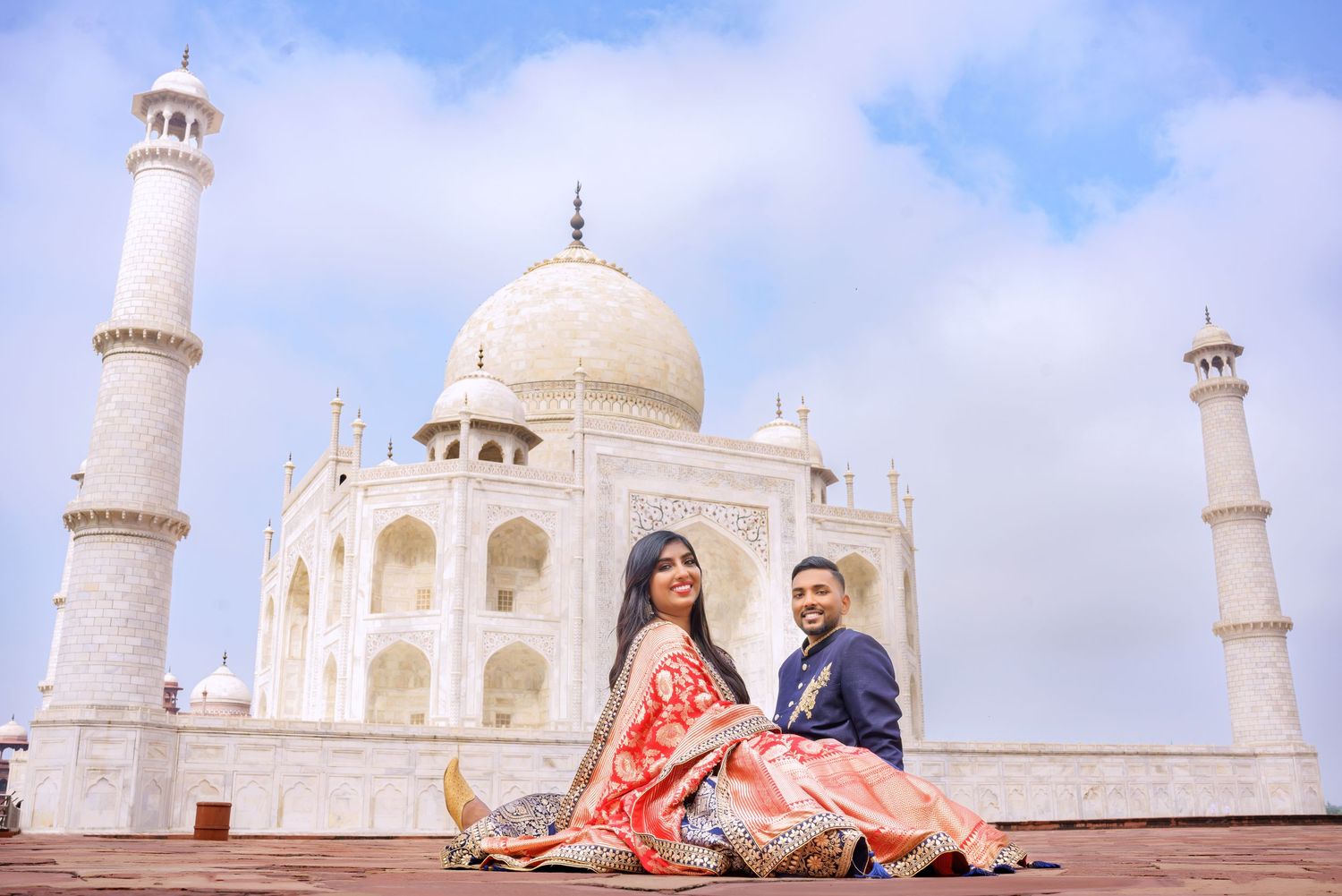 The iconic Taj Mahal monument photographed against a bright blue sky with white clouds.