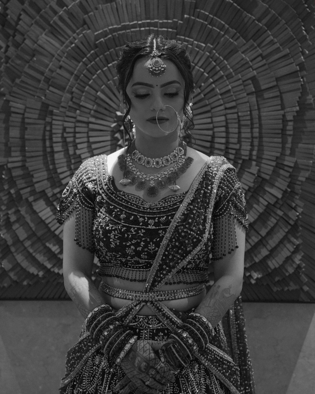 Black and white photo of a woman in ornate Indian bridal attire with jewelry and maang tikka.