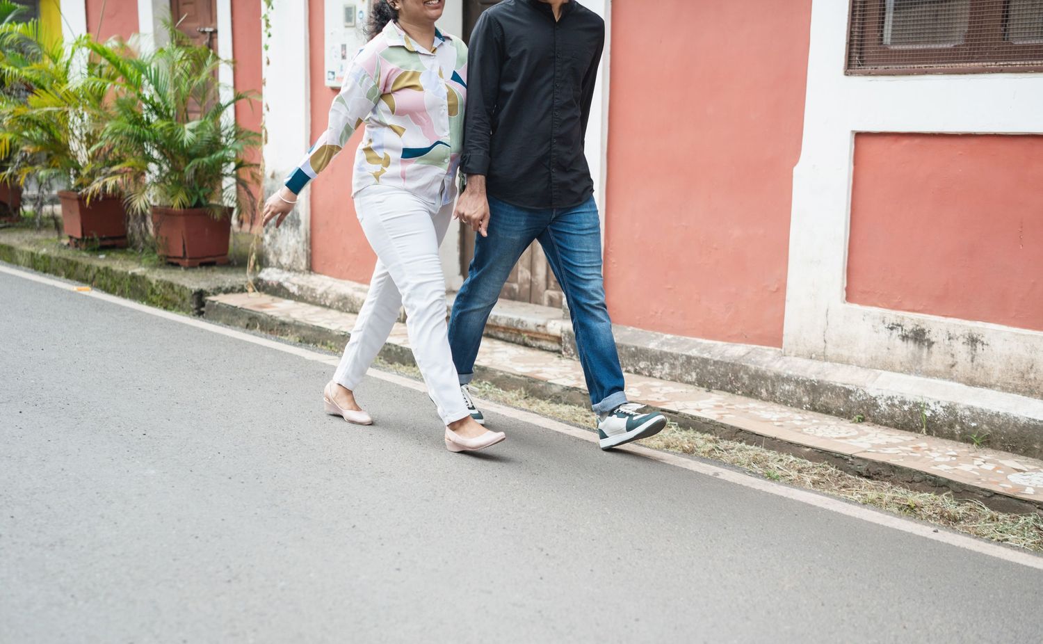 Two people walking past a pink colonial building on a street.
