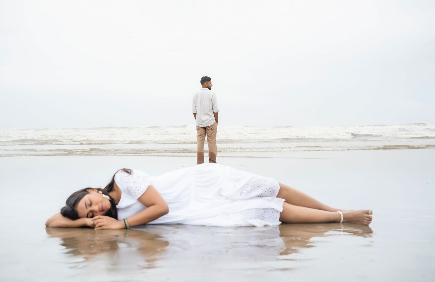 People lying on a sandy beach near the ocean waves on a bright day.