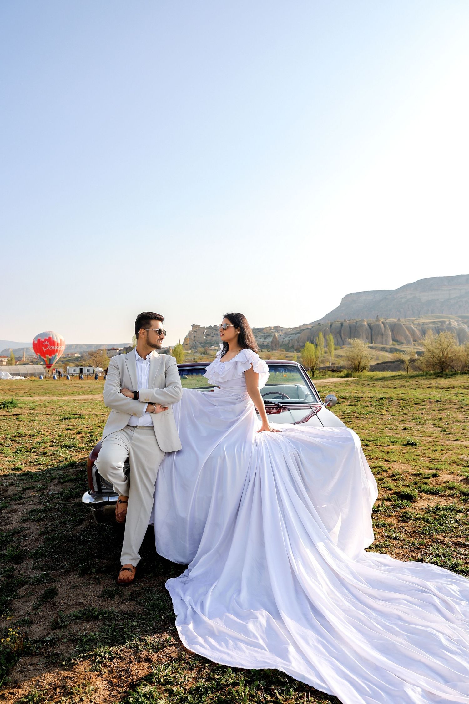 A flowing white wedding dress trails across an open field during a photo session.