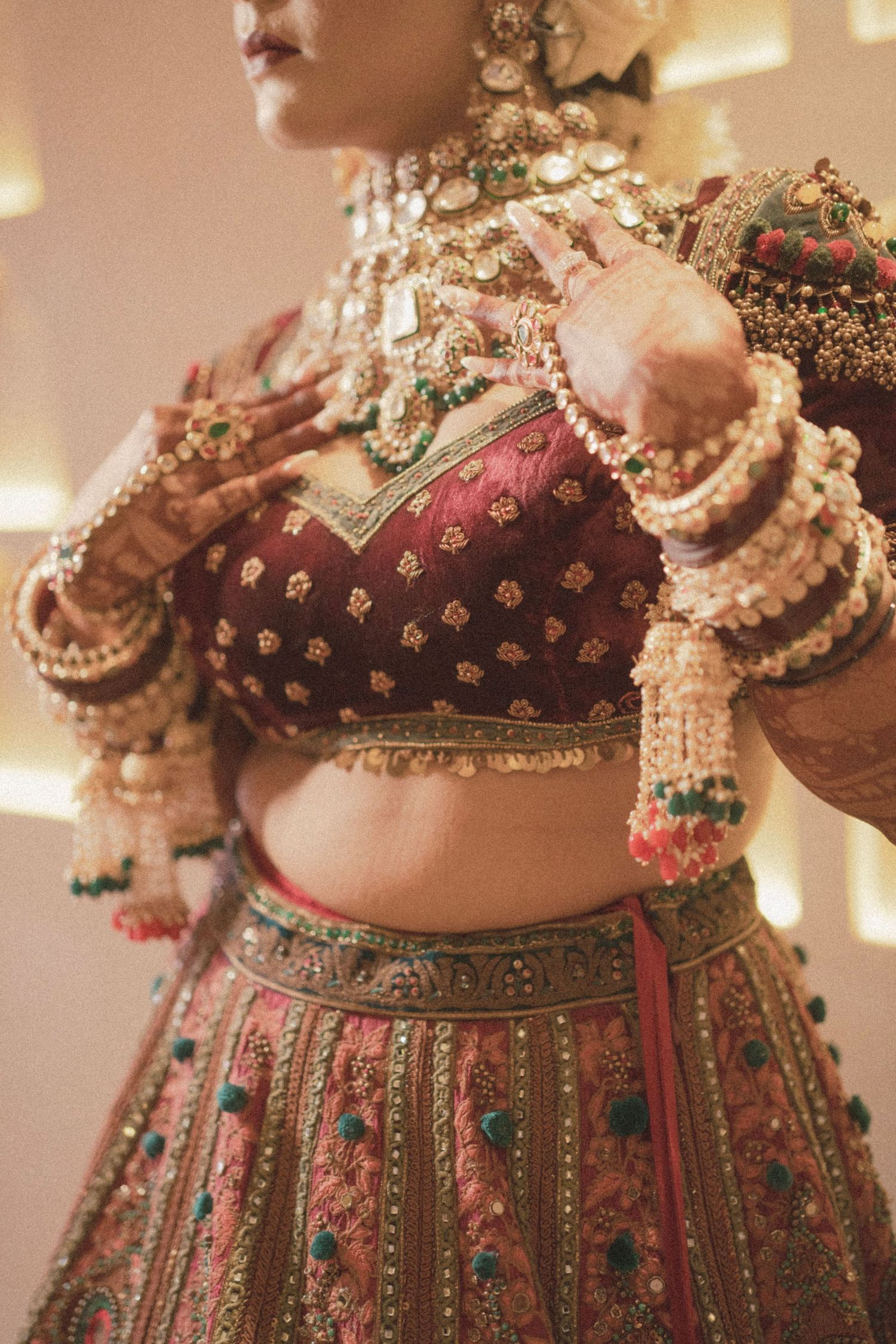 Indian bride in ornate red lehenga with gold embroidery, floral kalire bangles, and layered kundan jewelry.