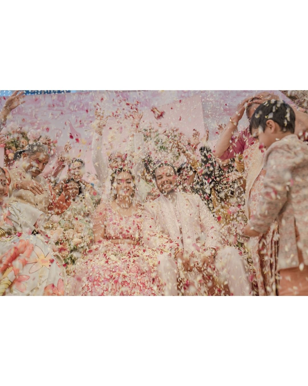 Colorful flower petals shower over bride and groom during joyful Indian wedding celebration ceremony.