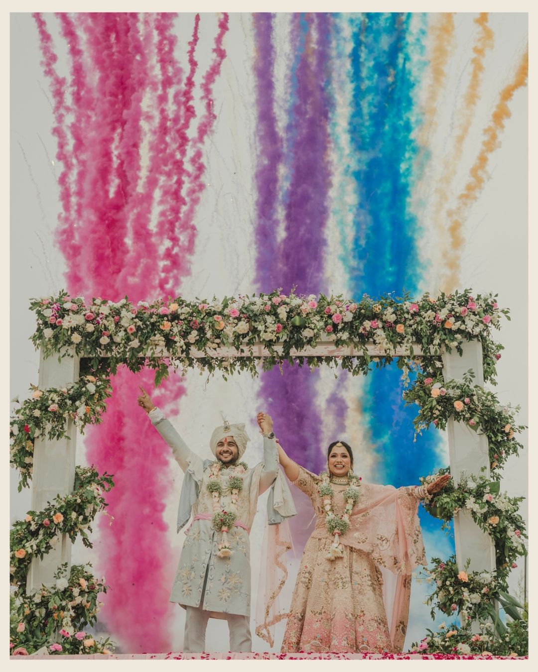 Sikh wedding couple celebrates under colorful smoke fountains and floral arch decorations.