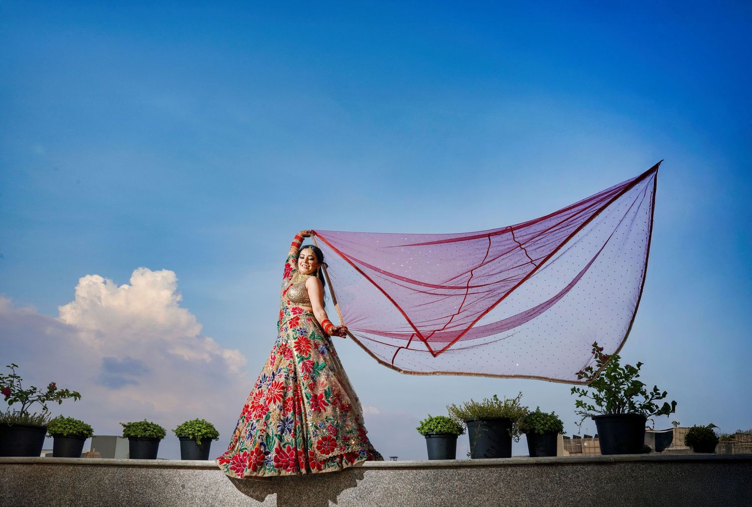 Outdoor bridal portraits with flowing veil against bright blue sky and white clouds.