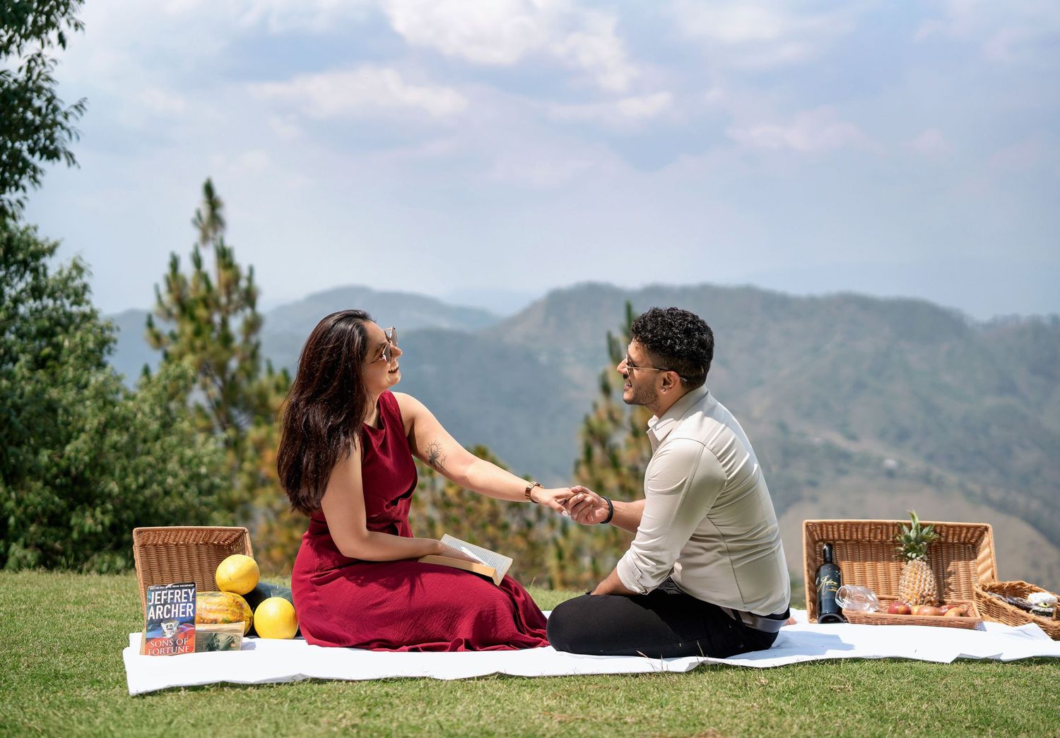 Couple enjoying a romantic picnic on a grassy hillside with mountain views in the background.