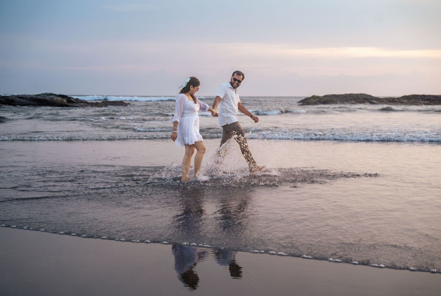 Two people splashing and playing in the ocean waves at sunset.