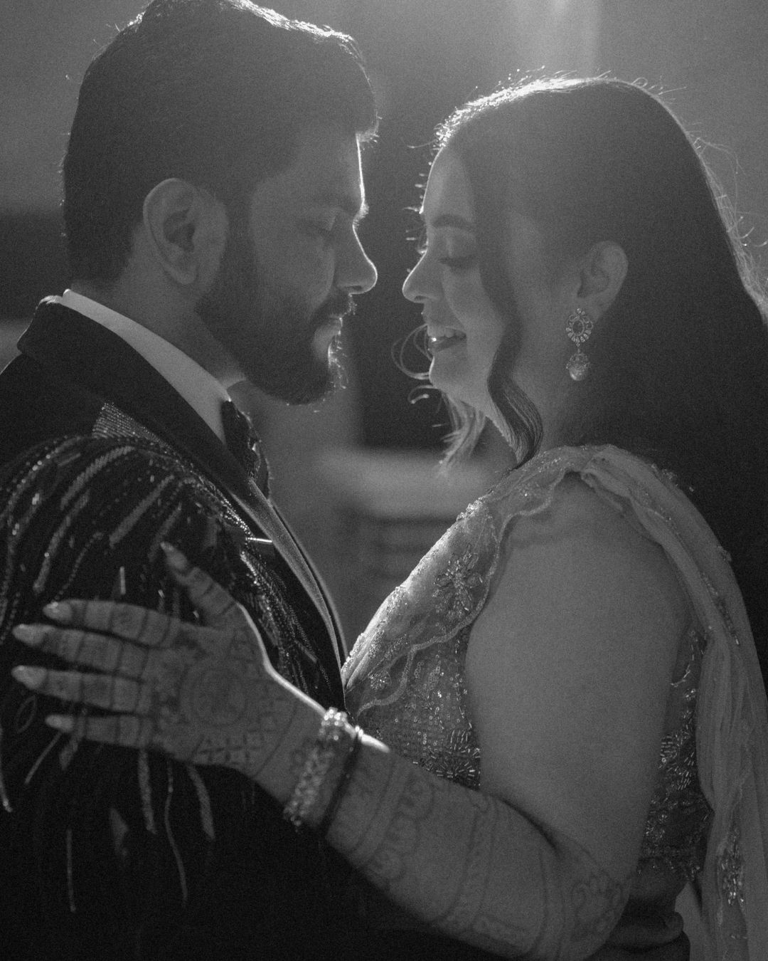 Black and white photo of a couple in traditional South Asian attire sharing a romantic moment at a wedding.