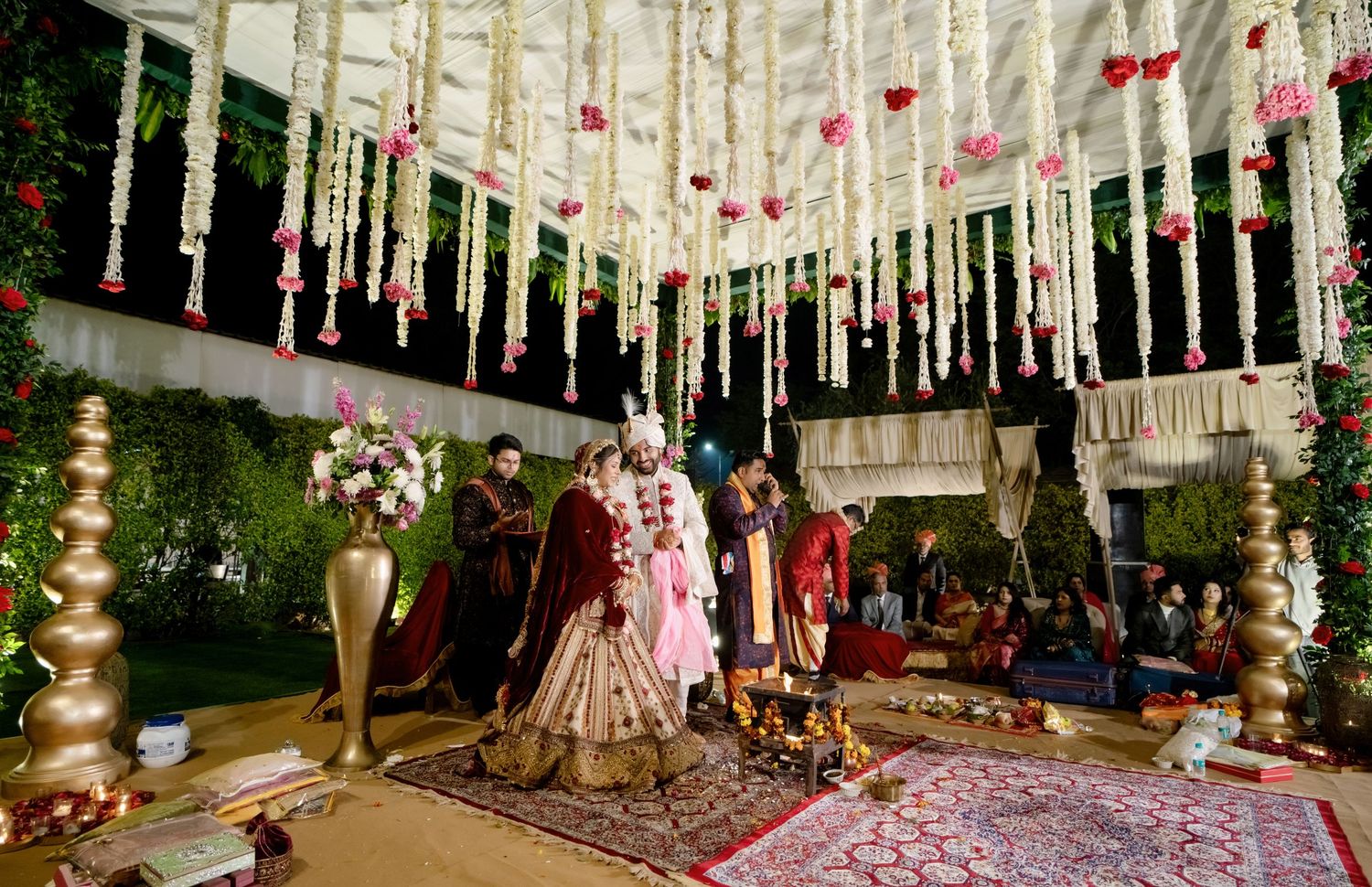 Elegant wedding venue decorated with pink and white florals and hanging fabric draping in a traditional Indian style setup.