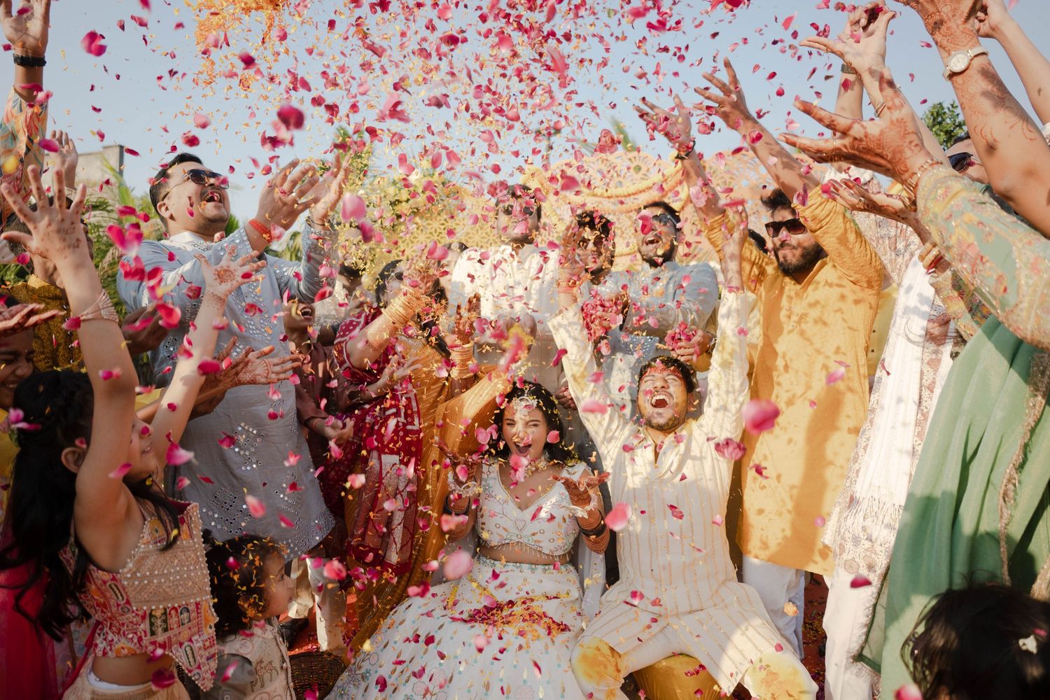Joyful Indian wedding celebration with colorful confetti and flower petals raining down on bride and groom.