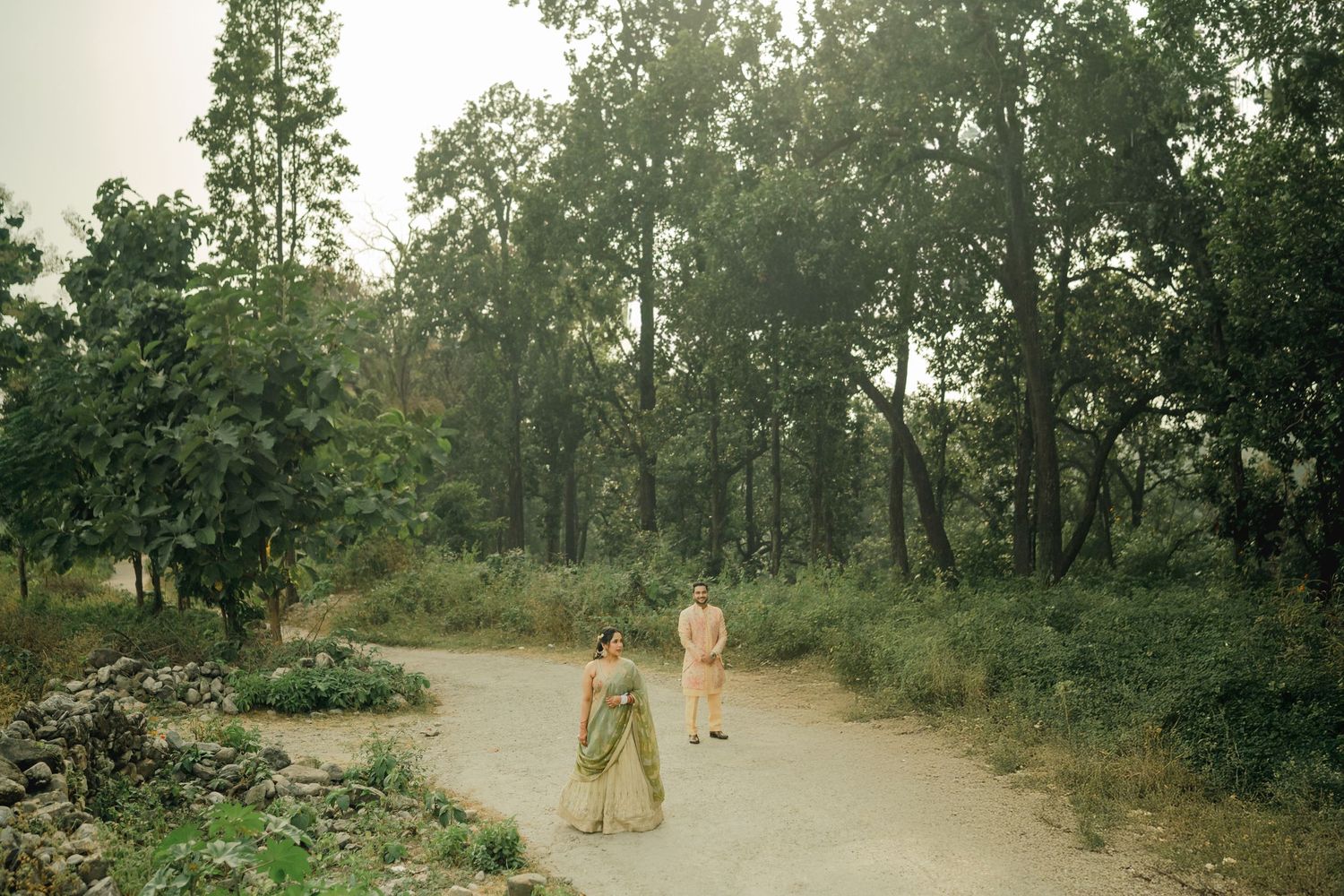A dirt path winds through a wooded area with figures walking along it in soft natural lighting.
