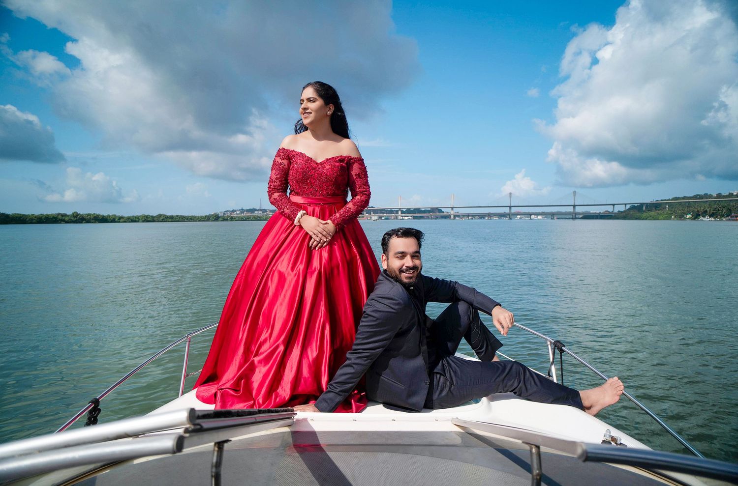 Woman in red gown and companion relaxing on luxury boat deck over calm waters.