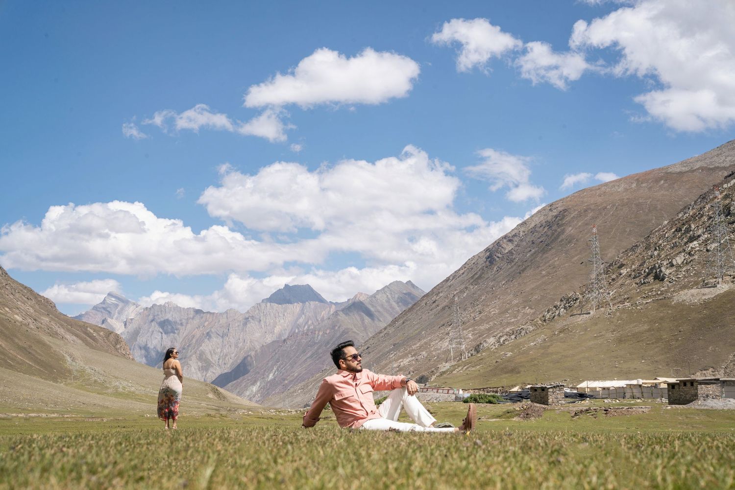 Dramatic mountain landscape with snow-capped peaks under puffy white clouds and blue skies.