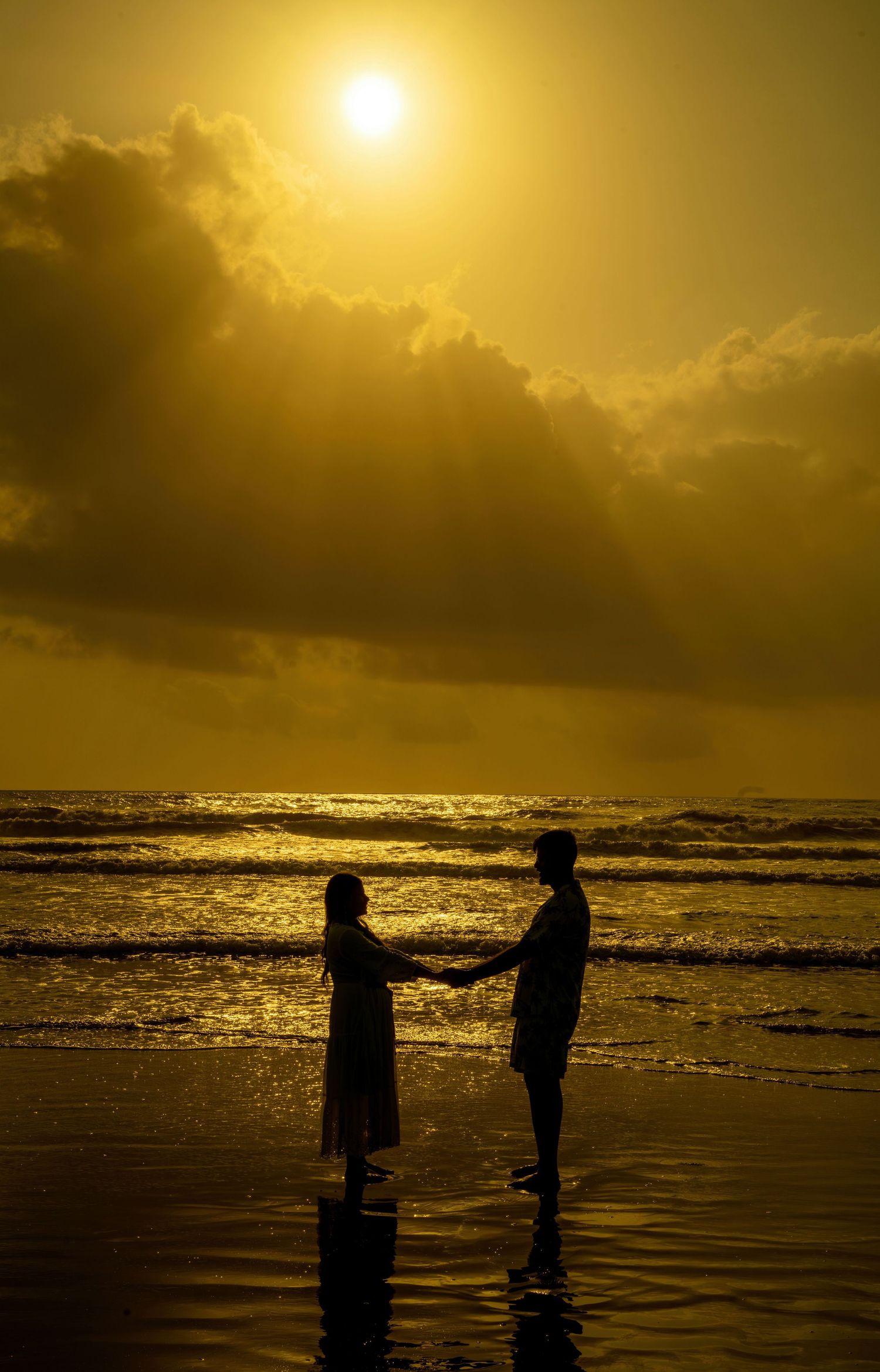 Silhouettes against golden sunset on beach with dramatic clouds and ocean waves.