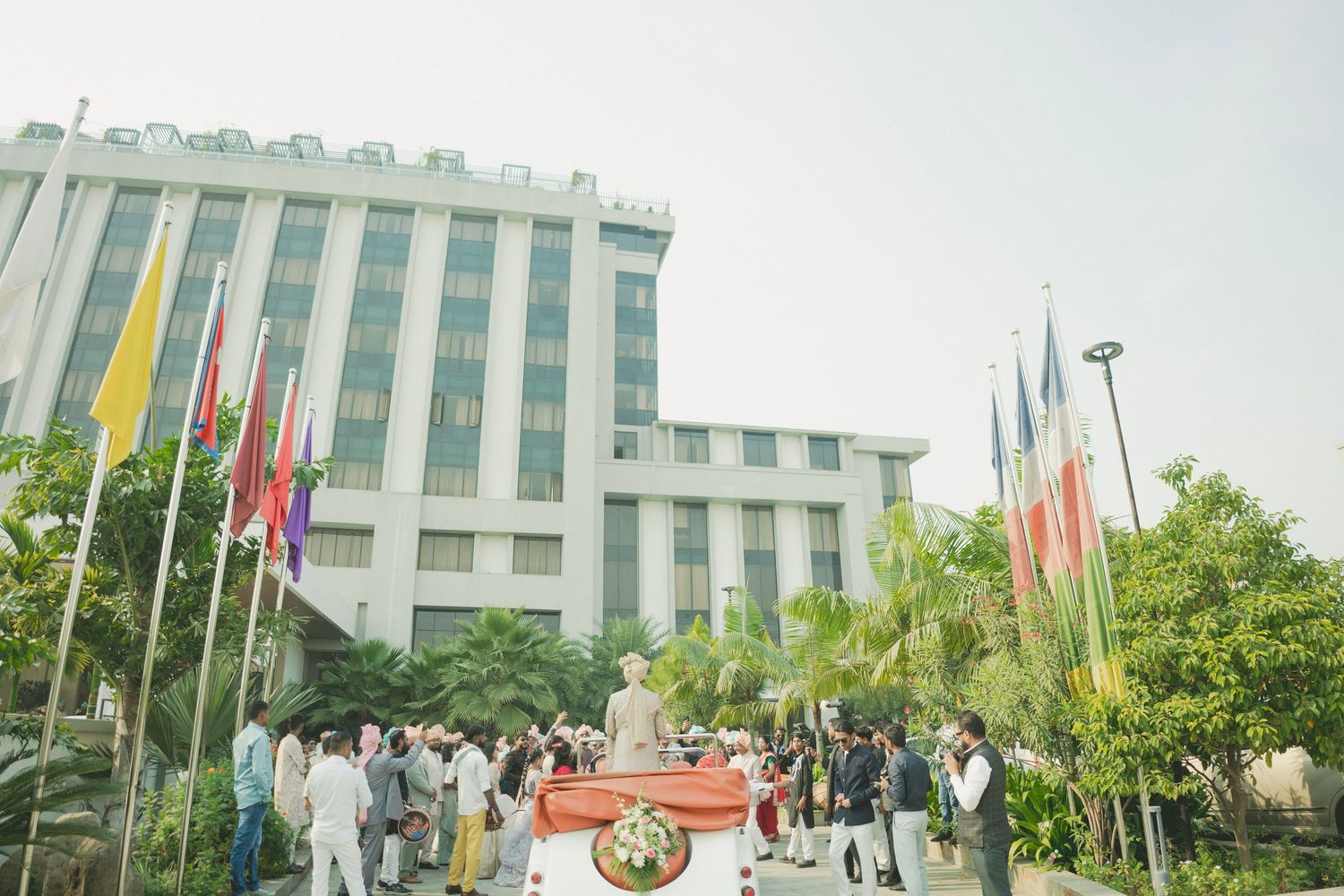 Crowd gathered outside a large hotel building with international flags displayed on poles during an outdoor ceremony.