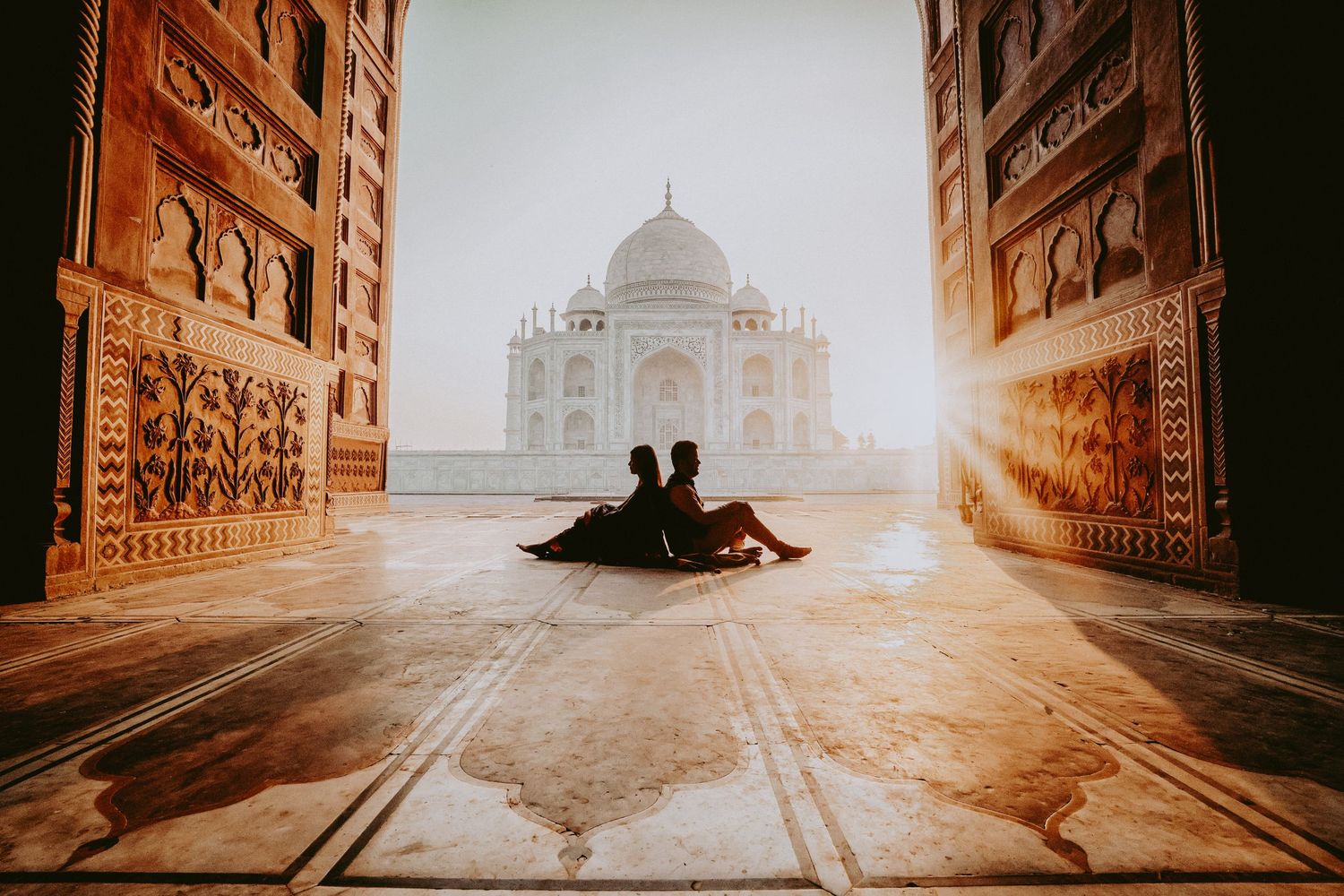 Couple sitting together at sunrise in front of the iconic Taj Mahal, bathed in golden light.