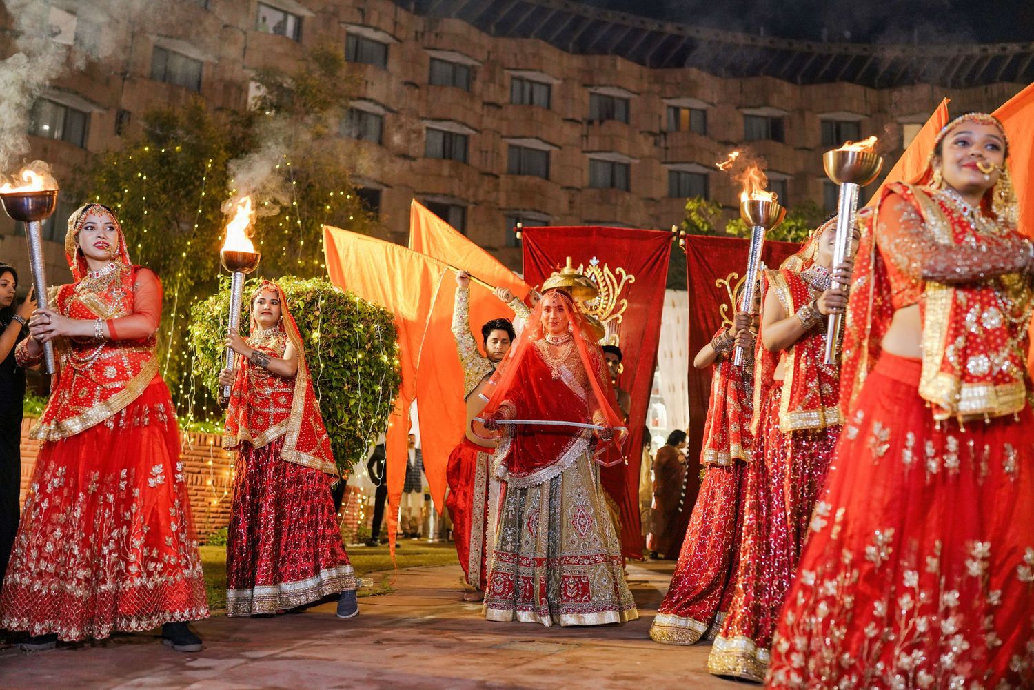 Row of traditional Indian wedding outfits in red and pink with intricate embroidery displayed outdoors.