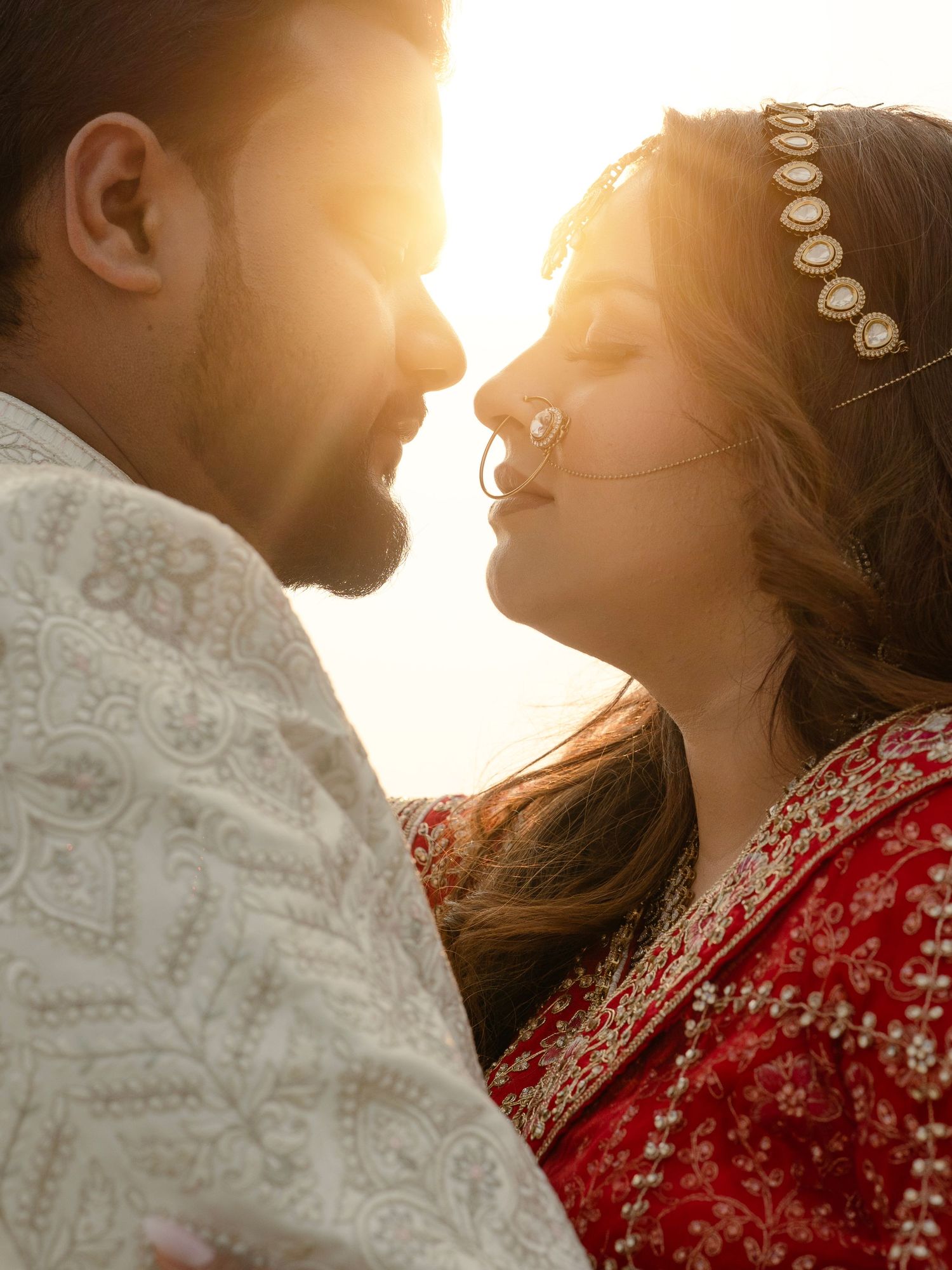 A couple in traditional South Asian wedding attire shares a romantic moment bathed in golden sunset light.