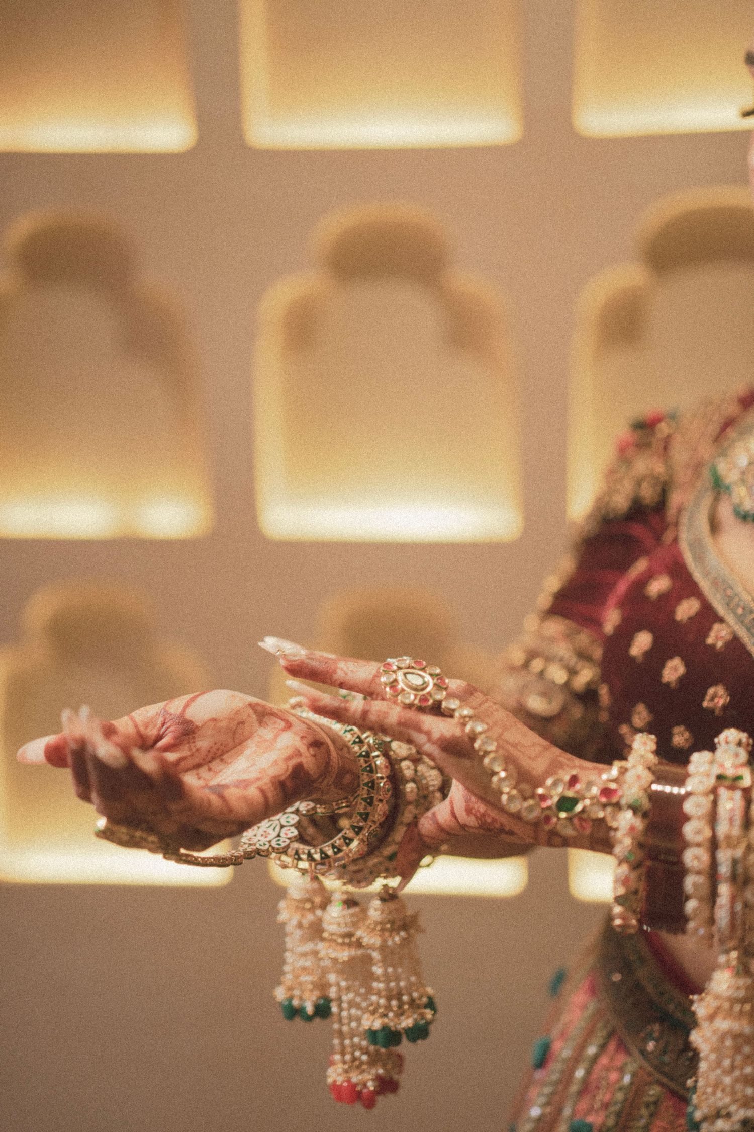 Indian bride's hands adorned with intricate mehndi, gold bangles, and floral kalire jewelry against ornate backdrop.