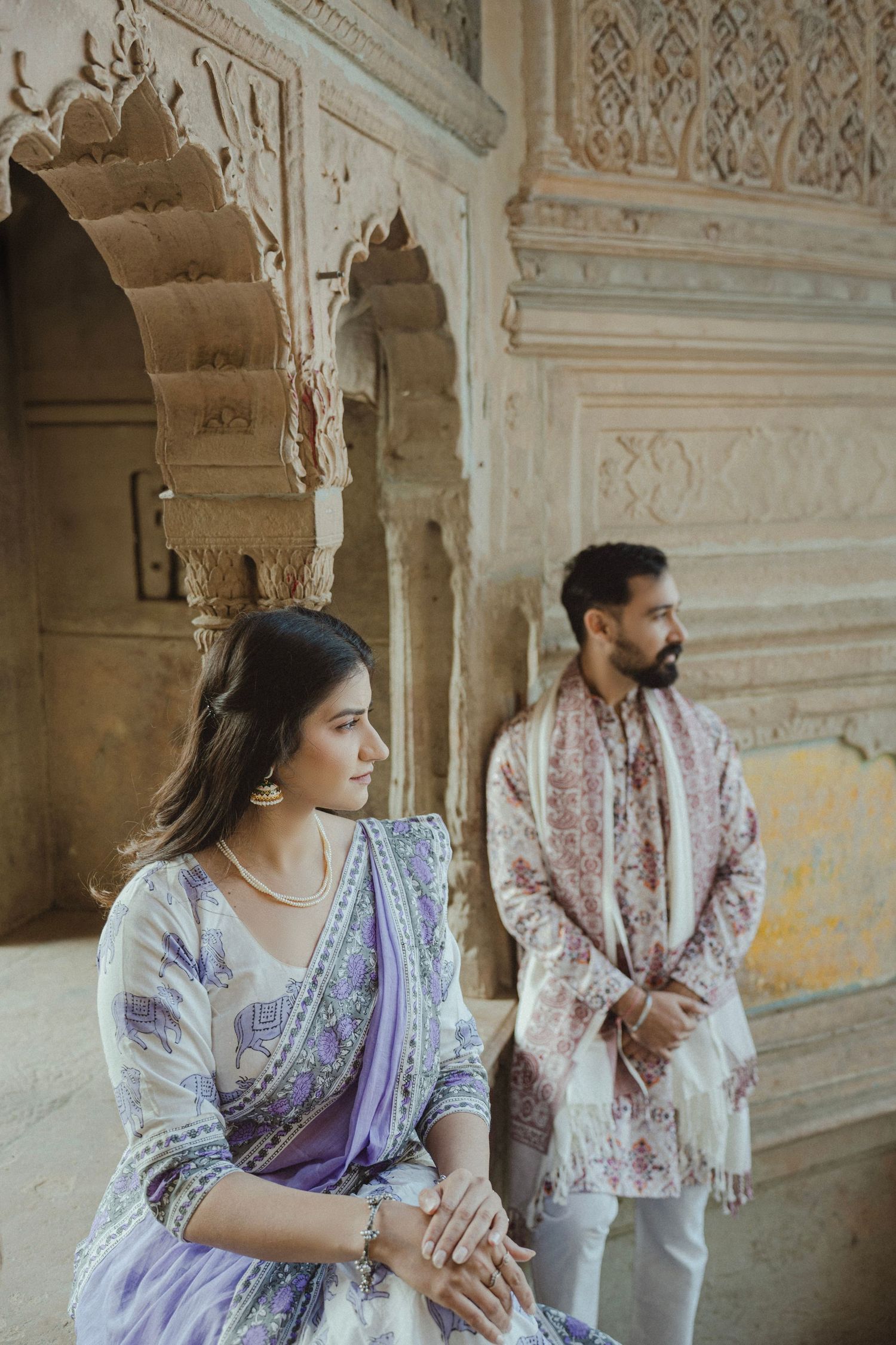 Couple in traditional Indian attire posing at an ornate heritage monument with intricate stone carvings.