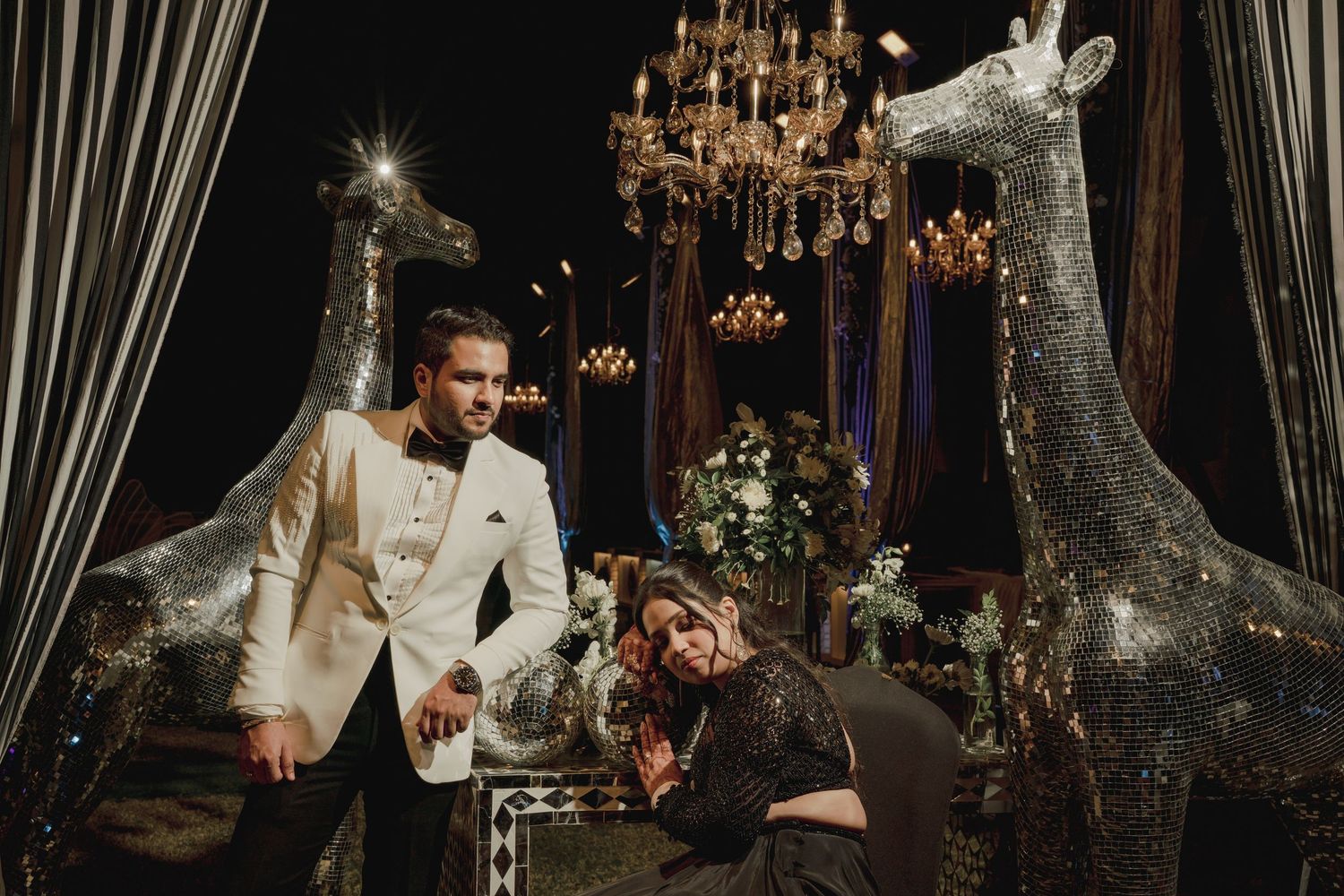 A romantic wedding couple poses in an elegant venue with ornate chandeliers and dramatic lighting.