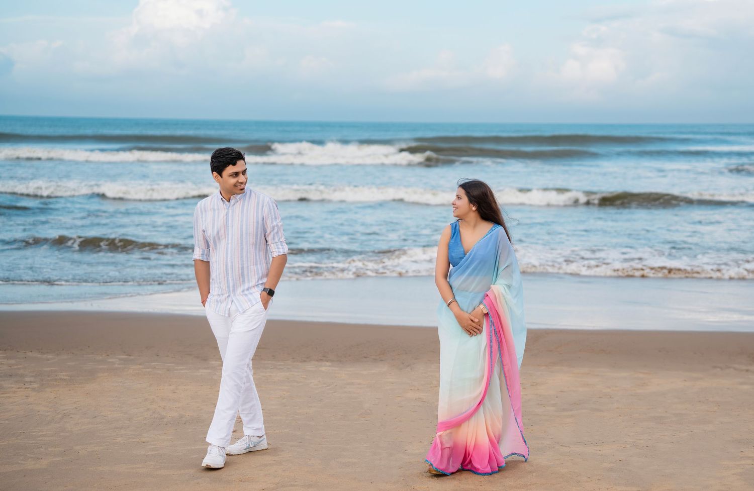 Couple sharing romantic moment on sandy beach with ocean waves in background.