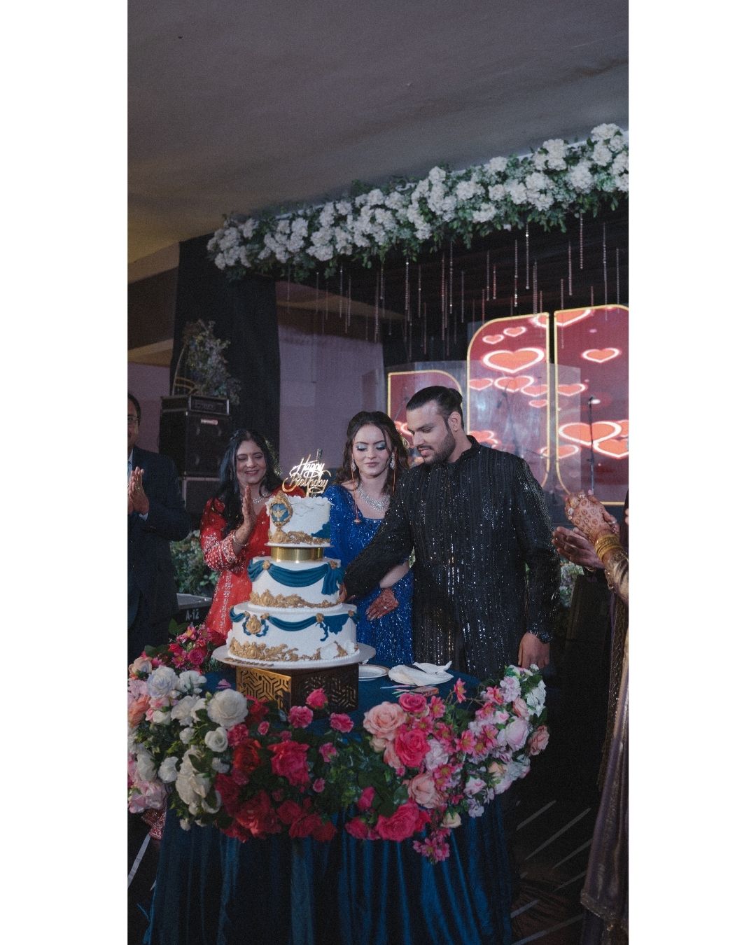 Couple cutting a multi-tier wedding cake surrounded by flowers at an elegant reception venue.