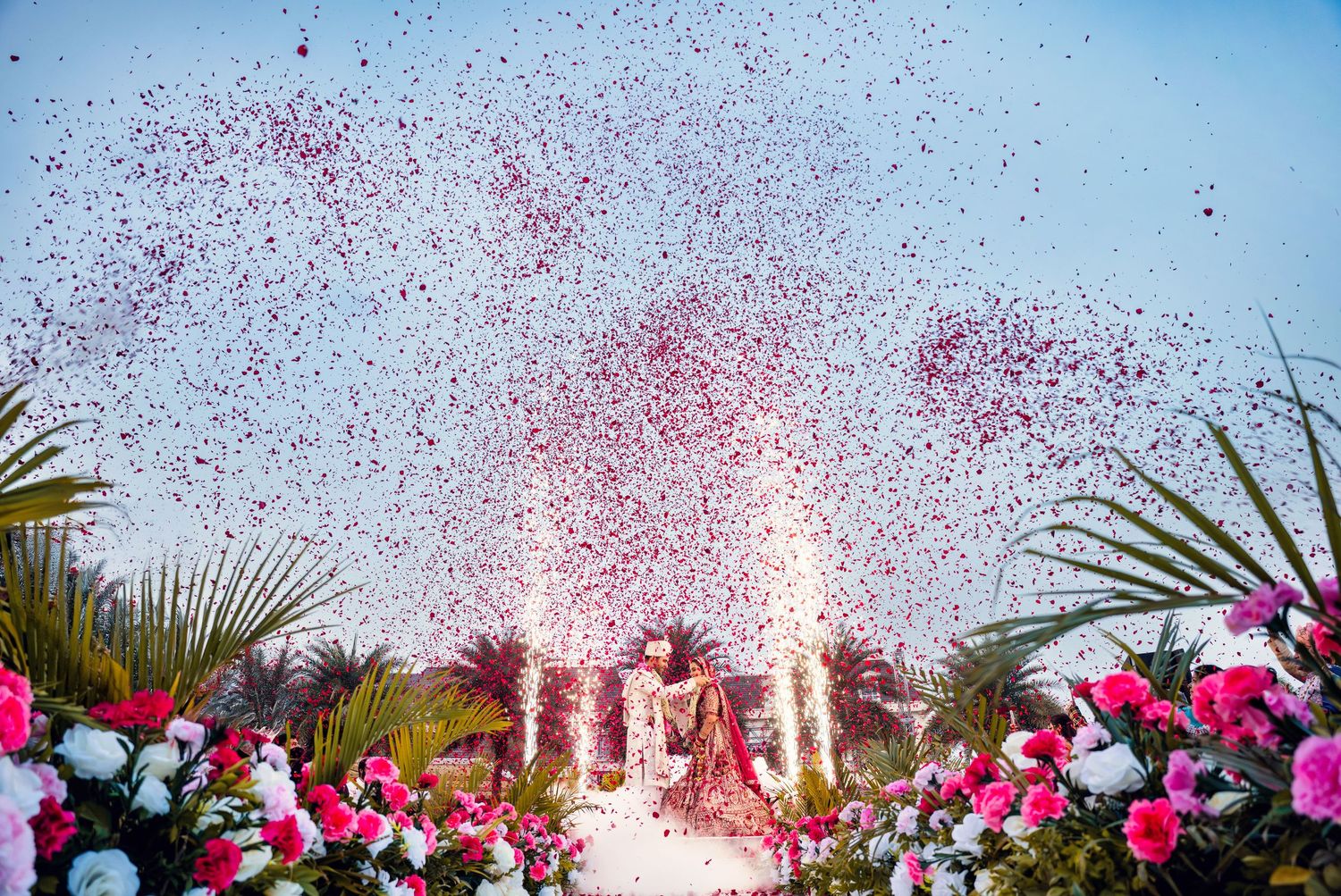 Outdoor celebration with pink and red confetti flying against bright blue sky.