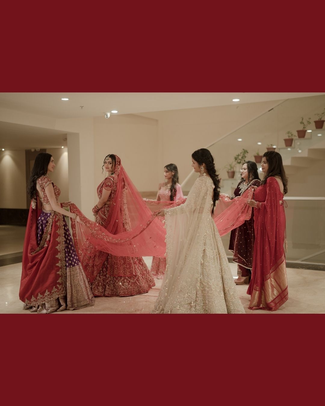 Women in traditional Indian attire prepare a bride in a white lehenga during a pre-wedding ceremony.