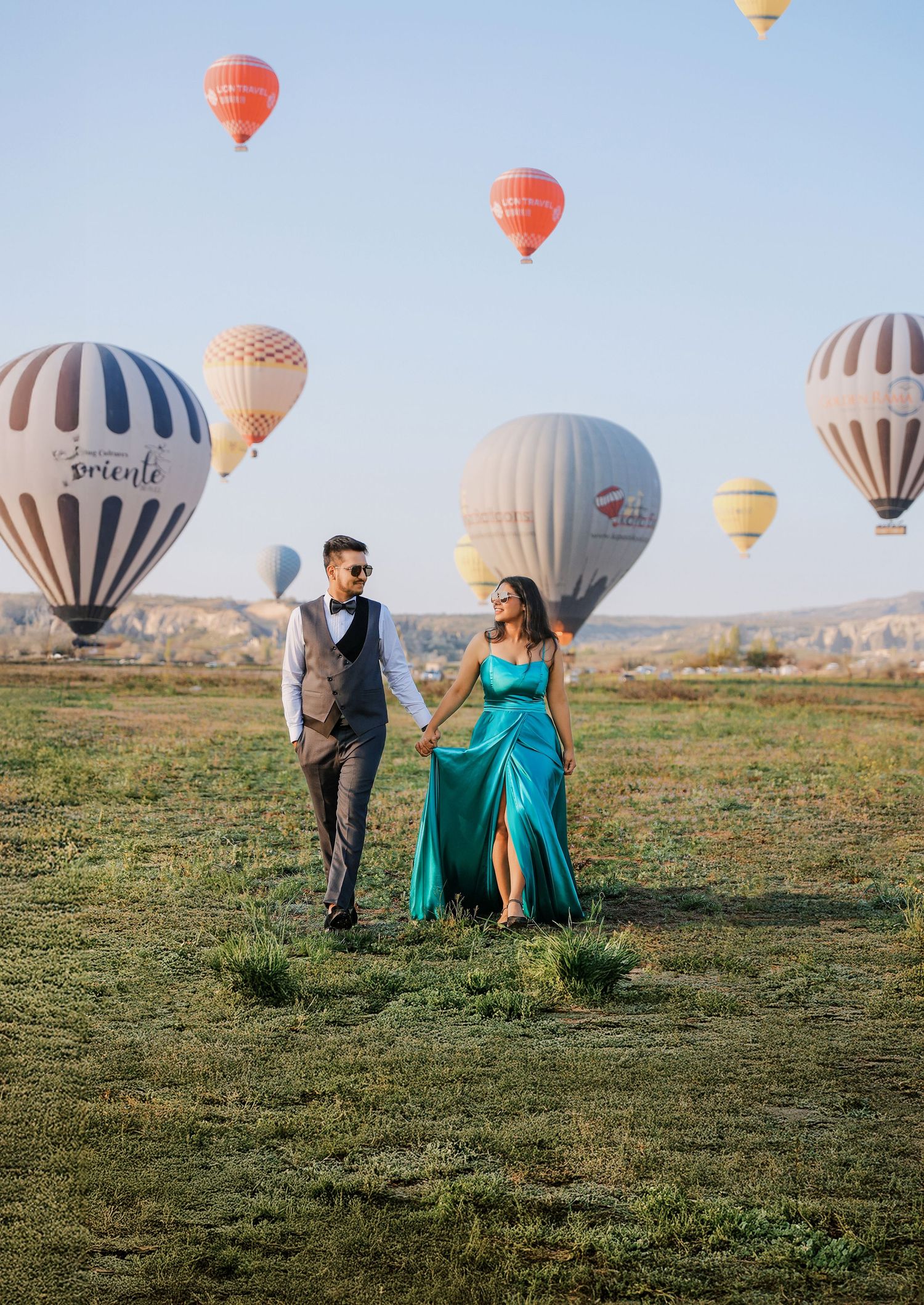 Hot air balloons dot the skyline in Cappadocia as couple poses in foreground.