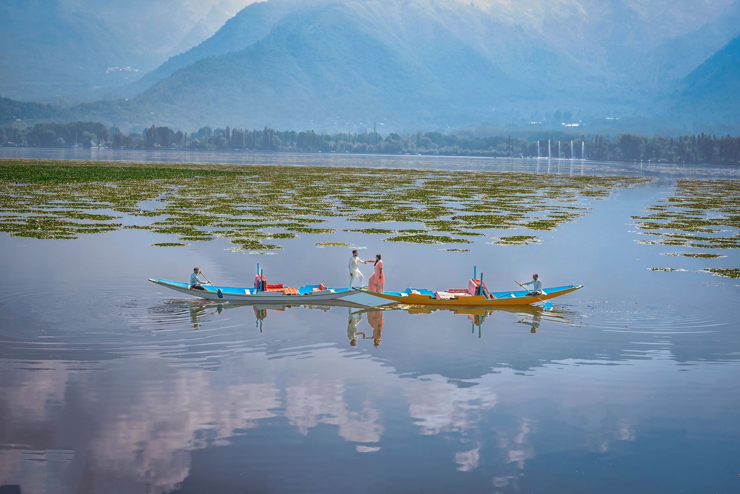 Row of colorful kayaks gliding across calm mountain lake with misty peaks in background.