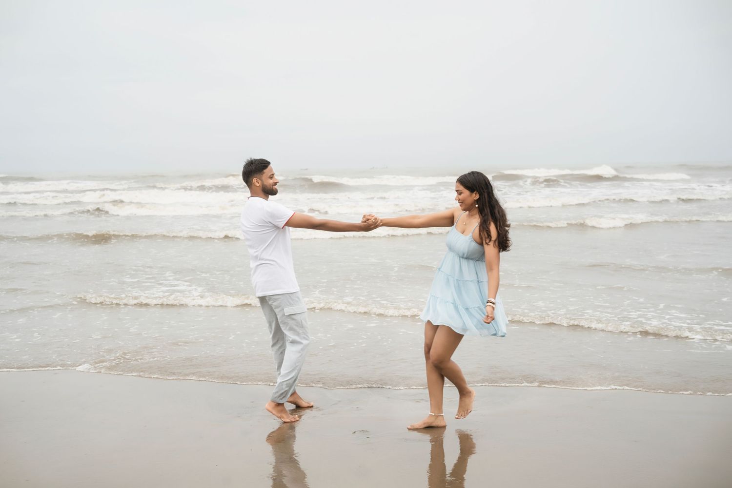 Romantic couple enjoying a playful moment at the beach in white outfits.