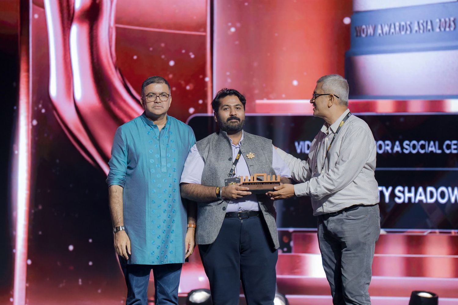 Stage presentation event with red backdrop and audience members in formal attire.